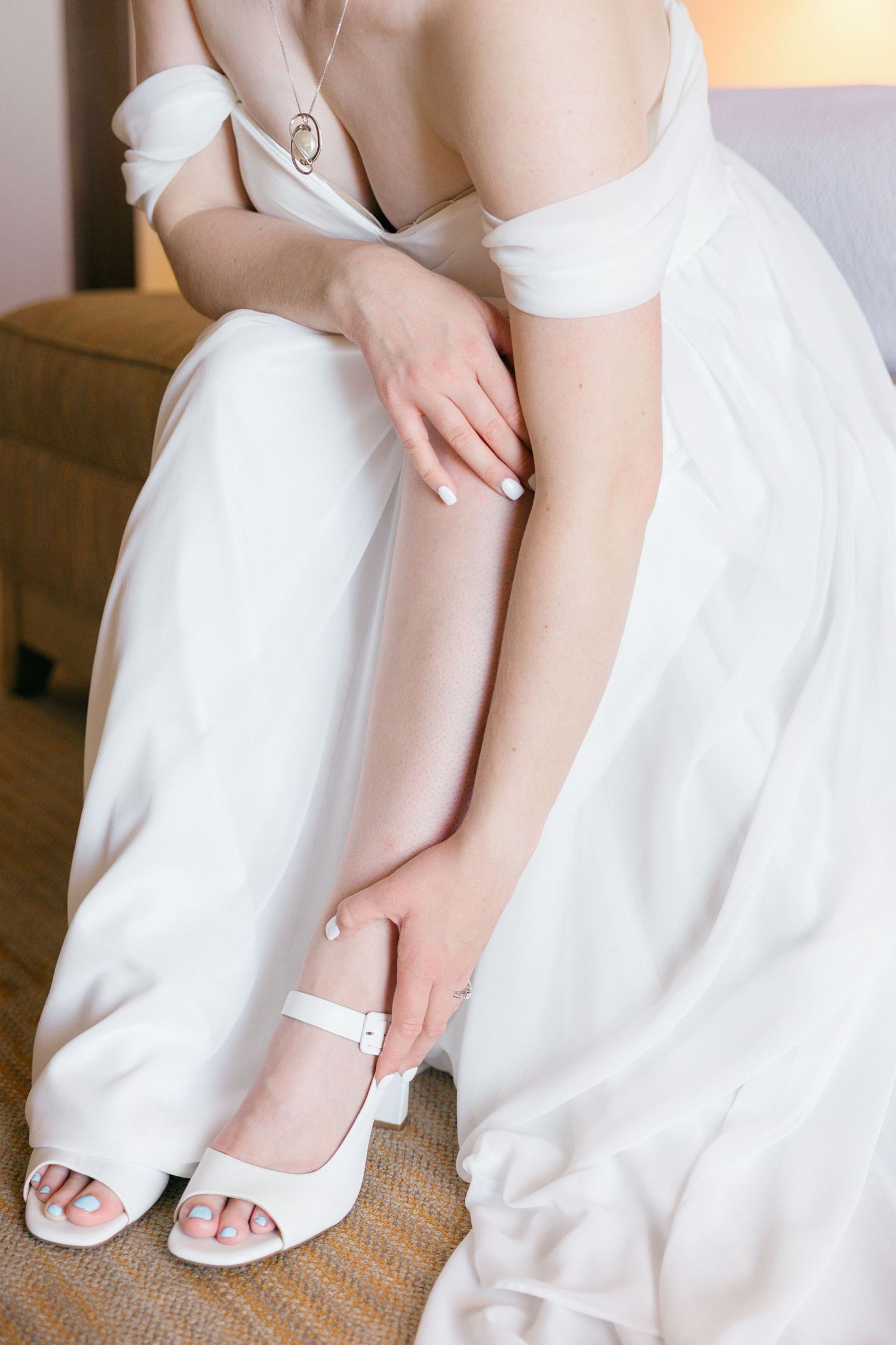 Close-up of white bridal shoes and dress hem on textured carpet.