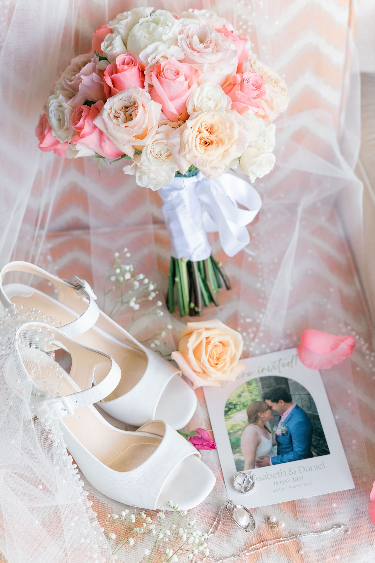 Bridal bouquet of pink and white roses with wedding shoes and photographs on tulle fabric.