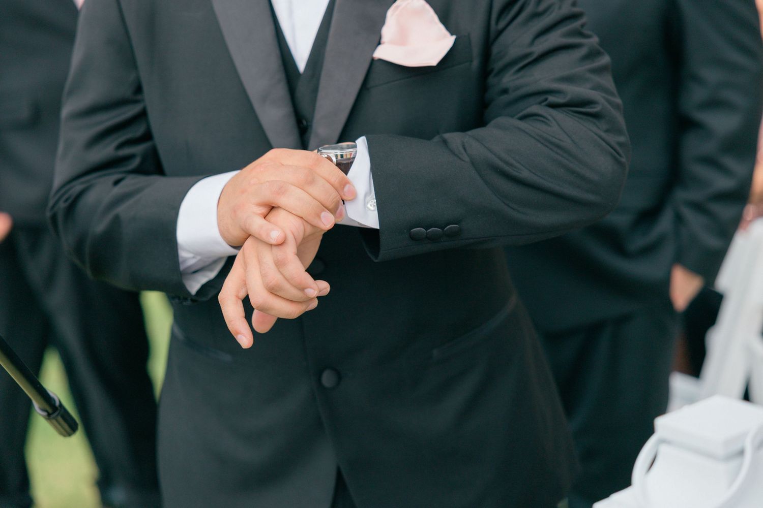 Close-up of groomsmen in black tuxedos during outdoor wedding ceremony.