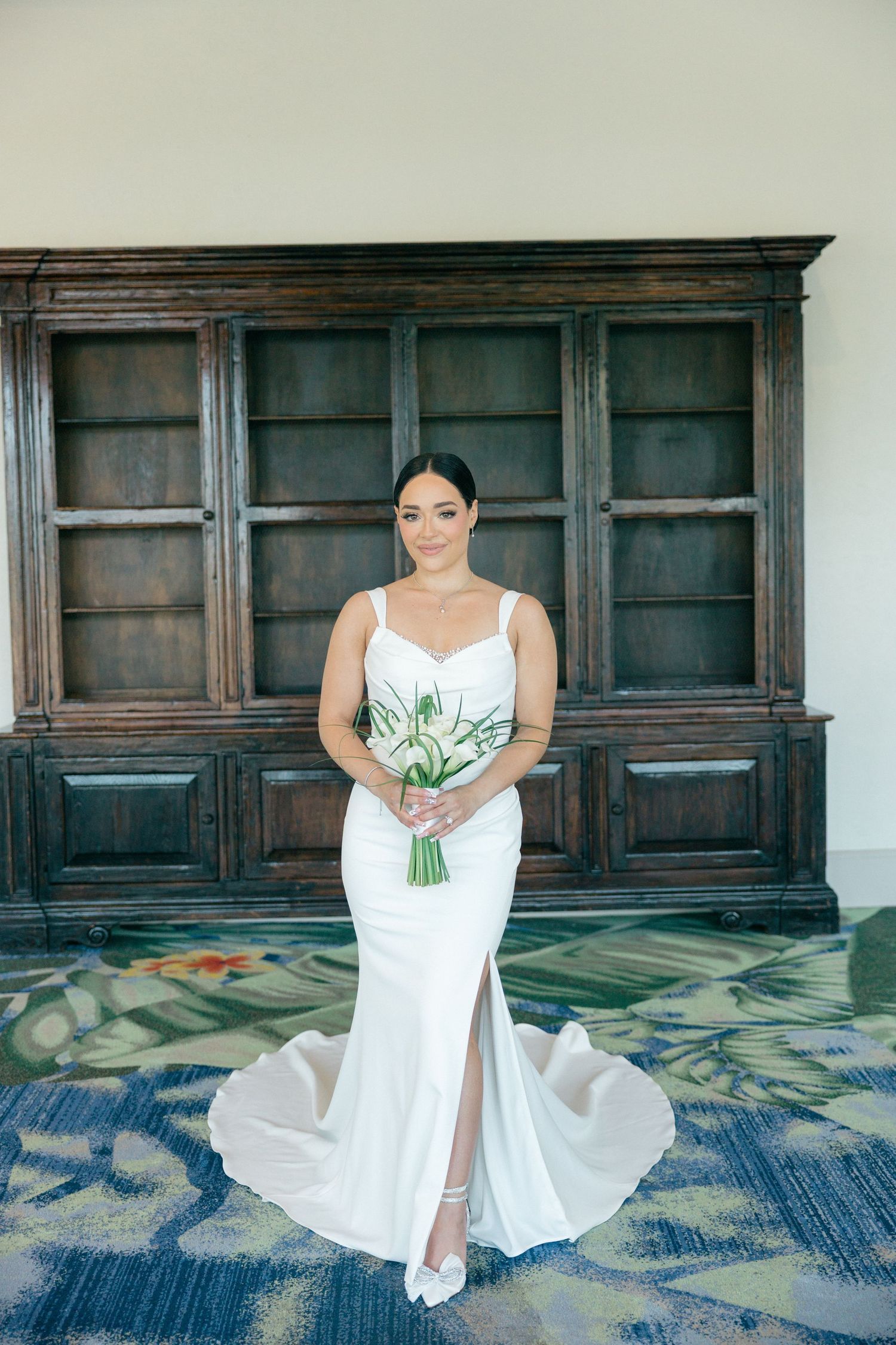 Bride in elegant white dress holds bouquet while posing in front of wooden panels.