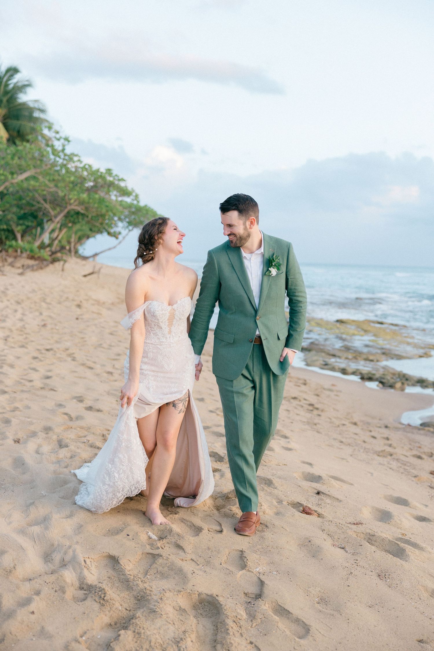 Couple walking along a scenic beach shoreline with waves and palm trees in the background.