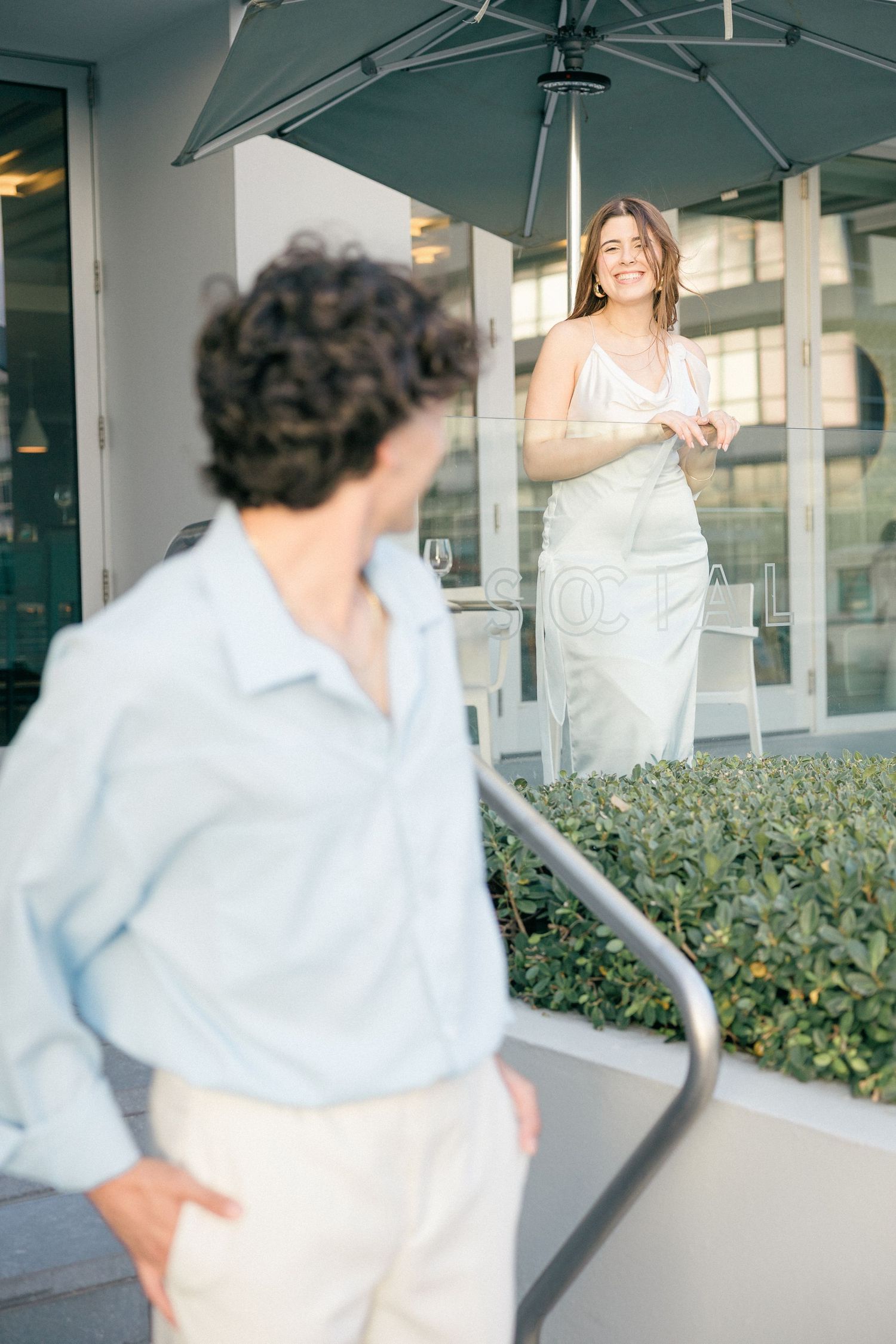 Playful couple dancing under a gray umbrella outside a modern building.