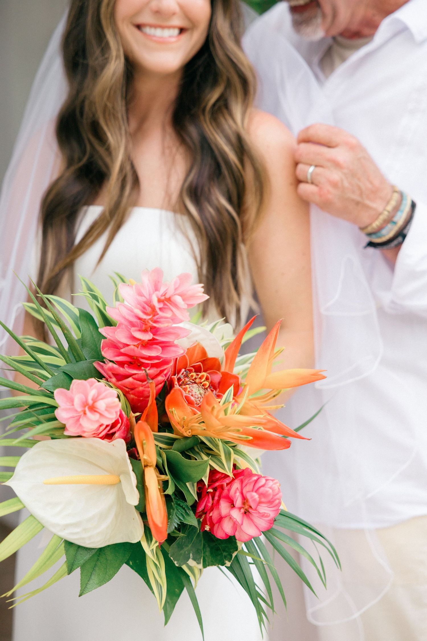 Tropical wedding bouquet with coral roses, birds of paradise, and green palm leaves.