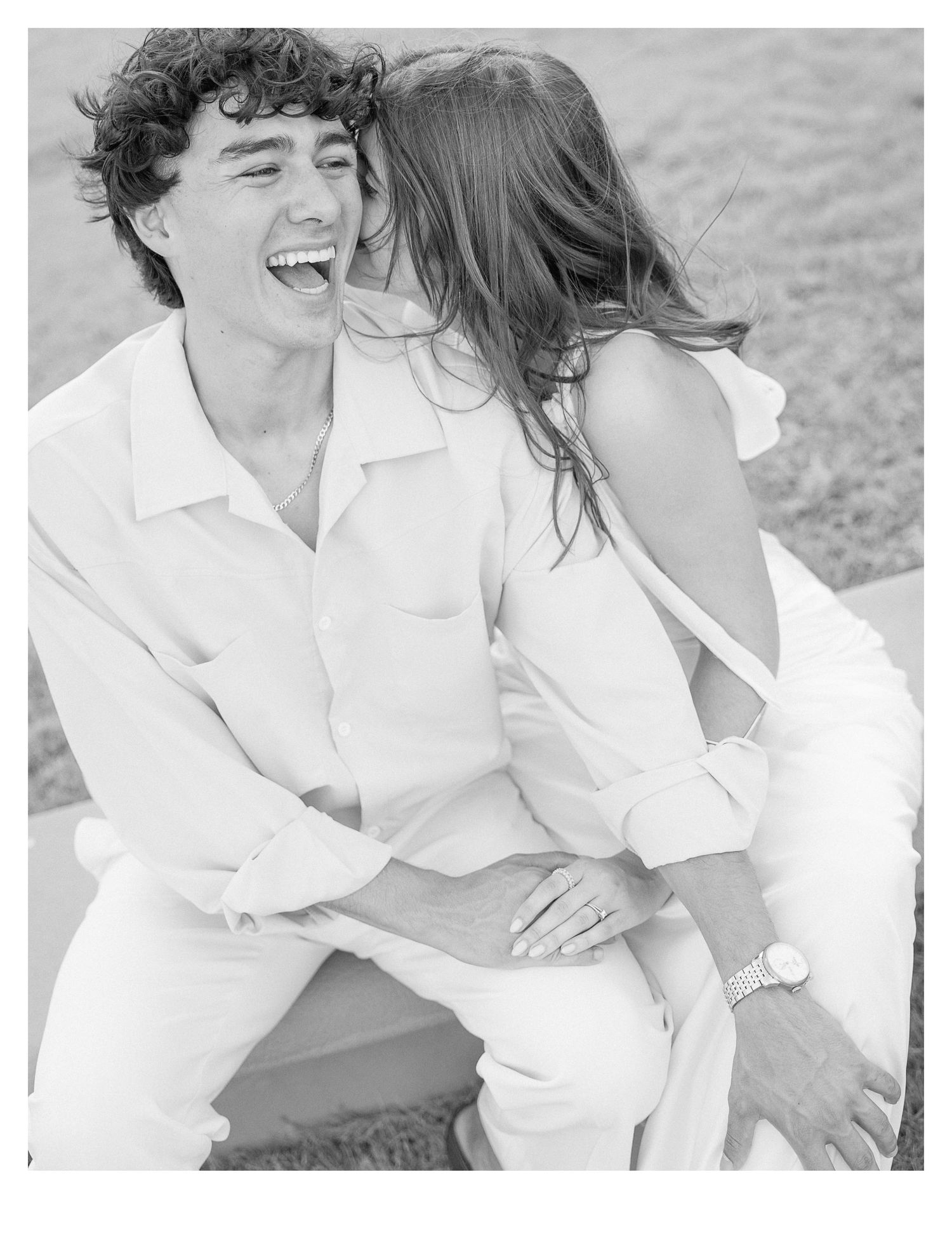 A couple in white clothing sharing an intimate black and white moment outdoors.