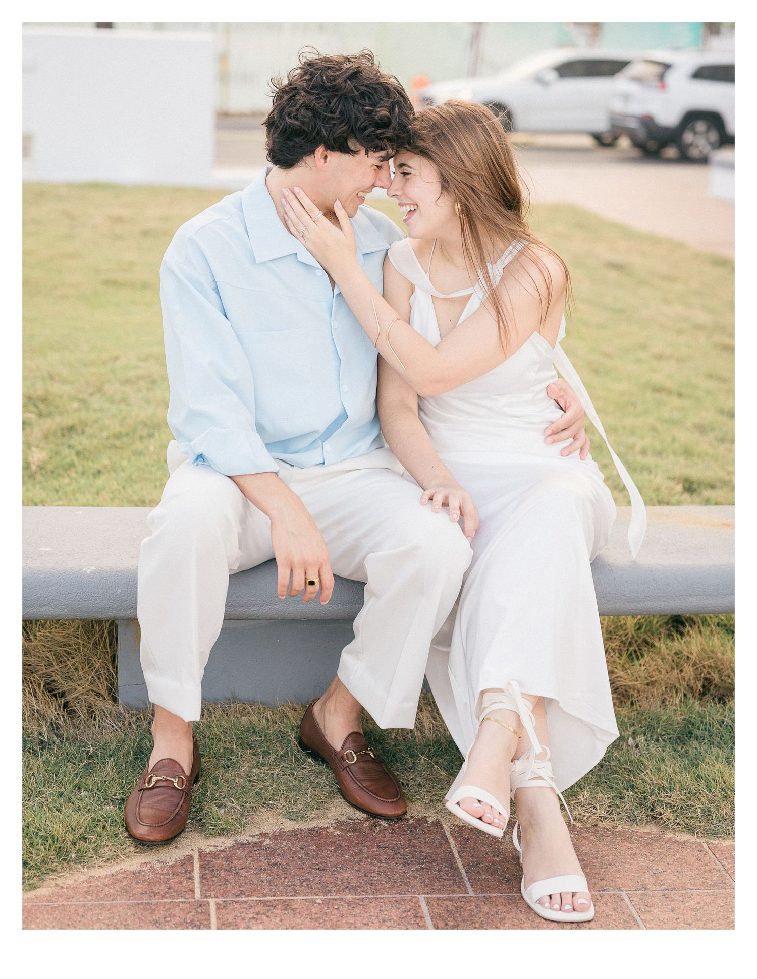 Couple sitting close together on a bench wearing coordinated white and light blue outfits.