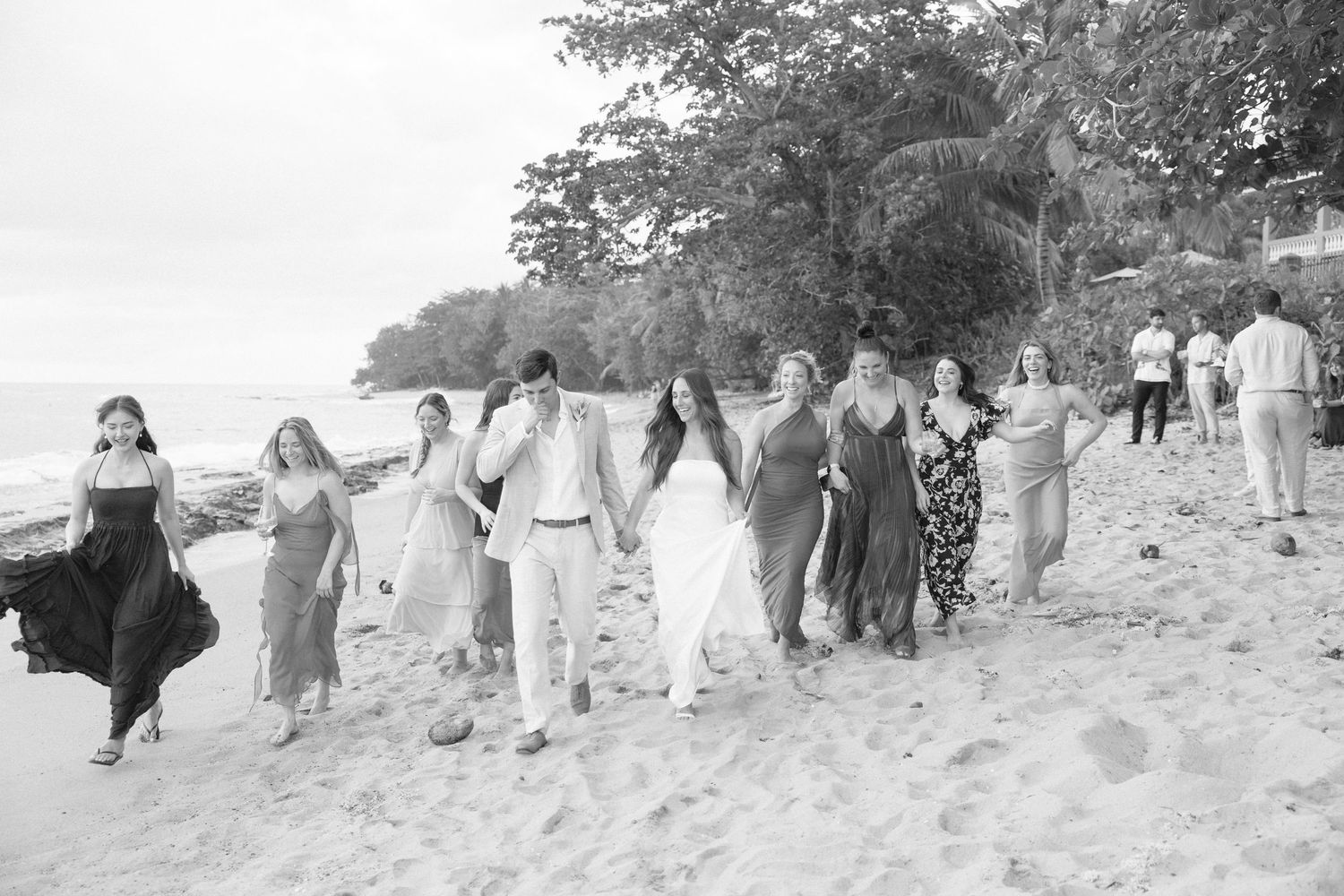 A large group walks along a scenic beach path in coordinated outfits during a photo session.