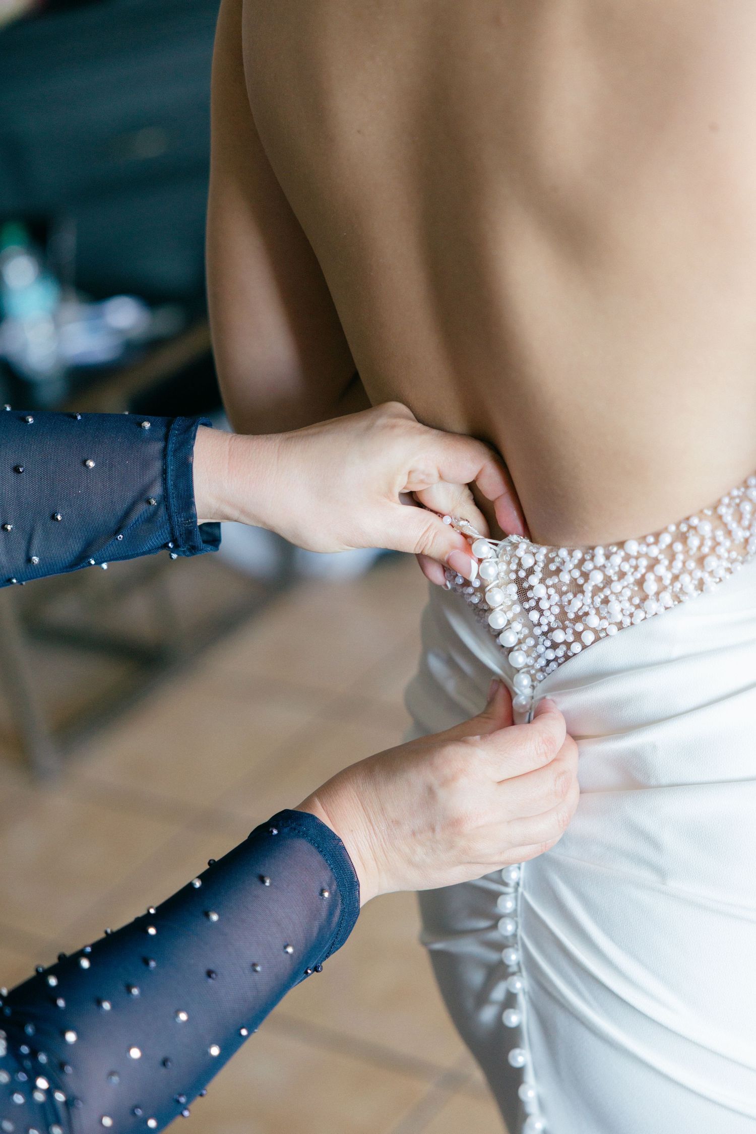 Close-up of hands adjusting a white wedding dress with delicate beaded details on navy blue fabric.