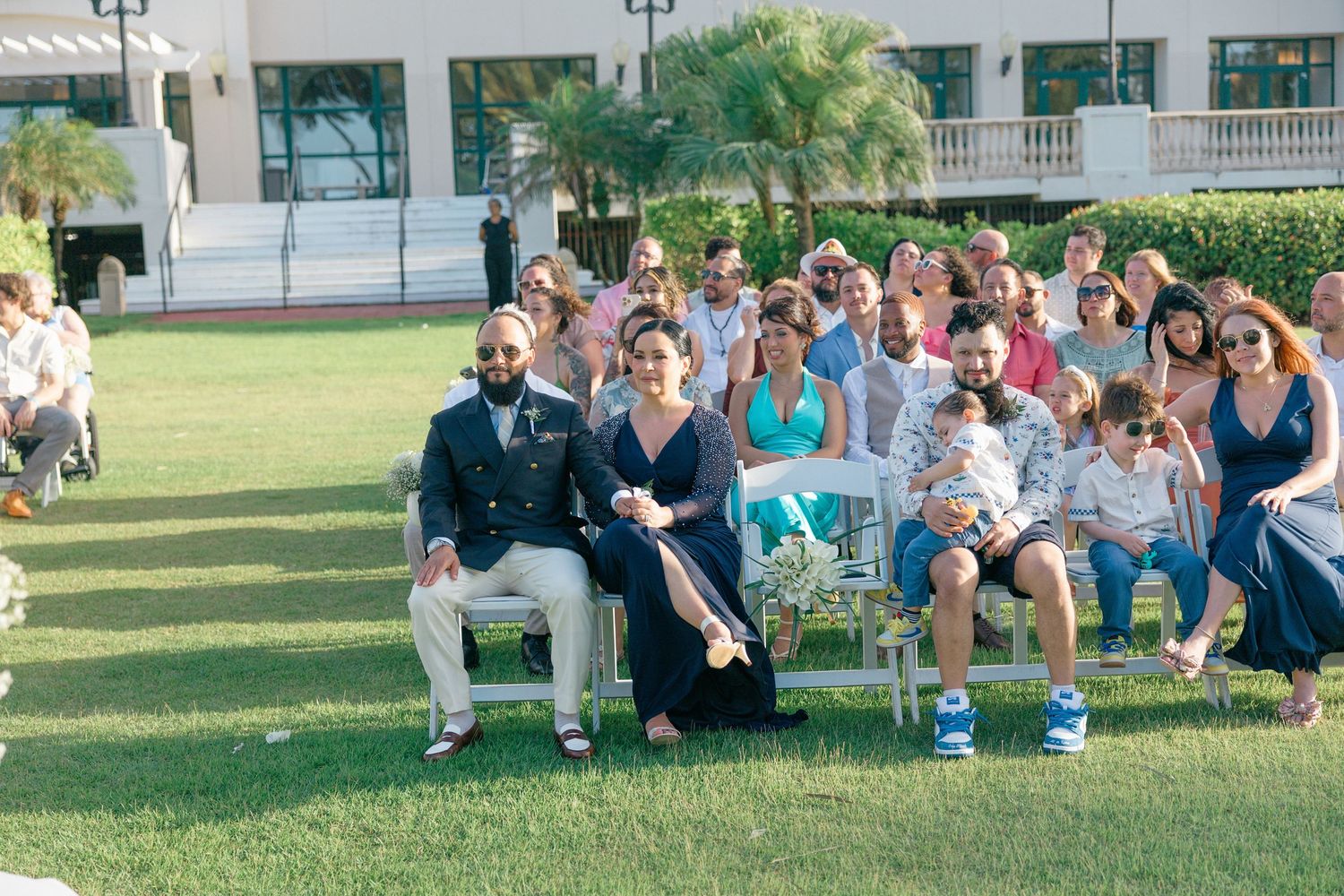 Wedding guests seated on lawn watching outdoor ceremony proceedings.