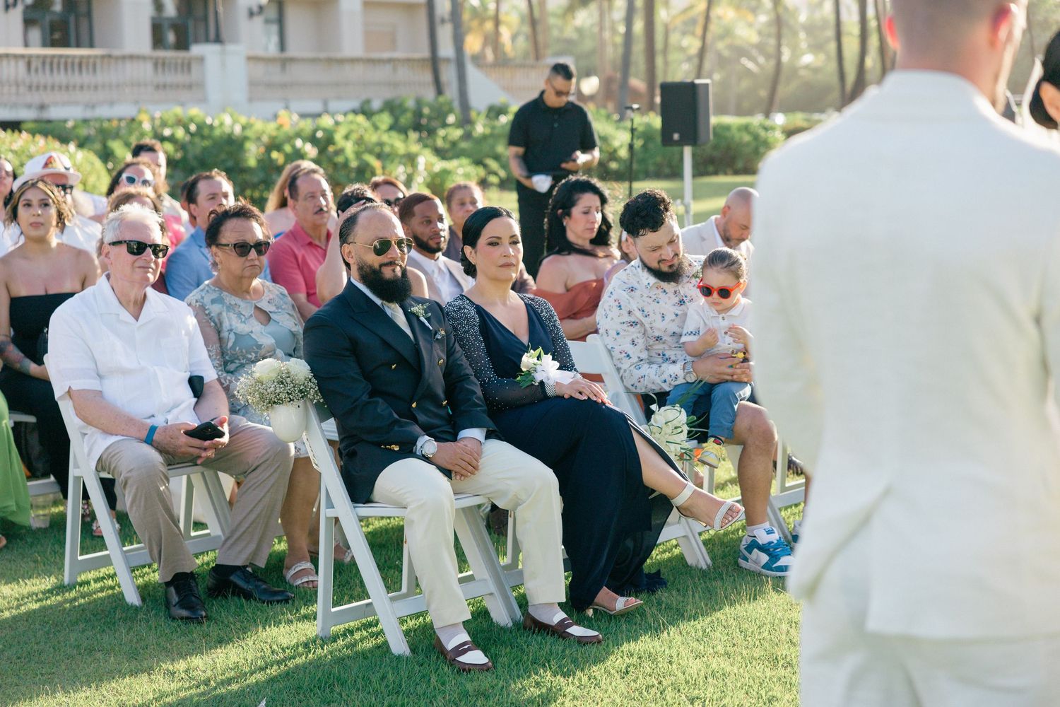 Wedding guests seated on lawn chairs during outdoor garden ceremony.