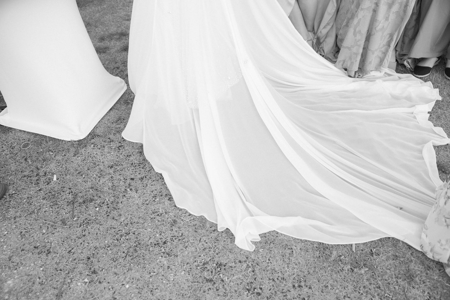 Flowing white wedding dress train draped elegantly across outdoor ground.