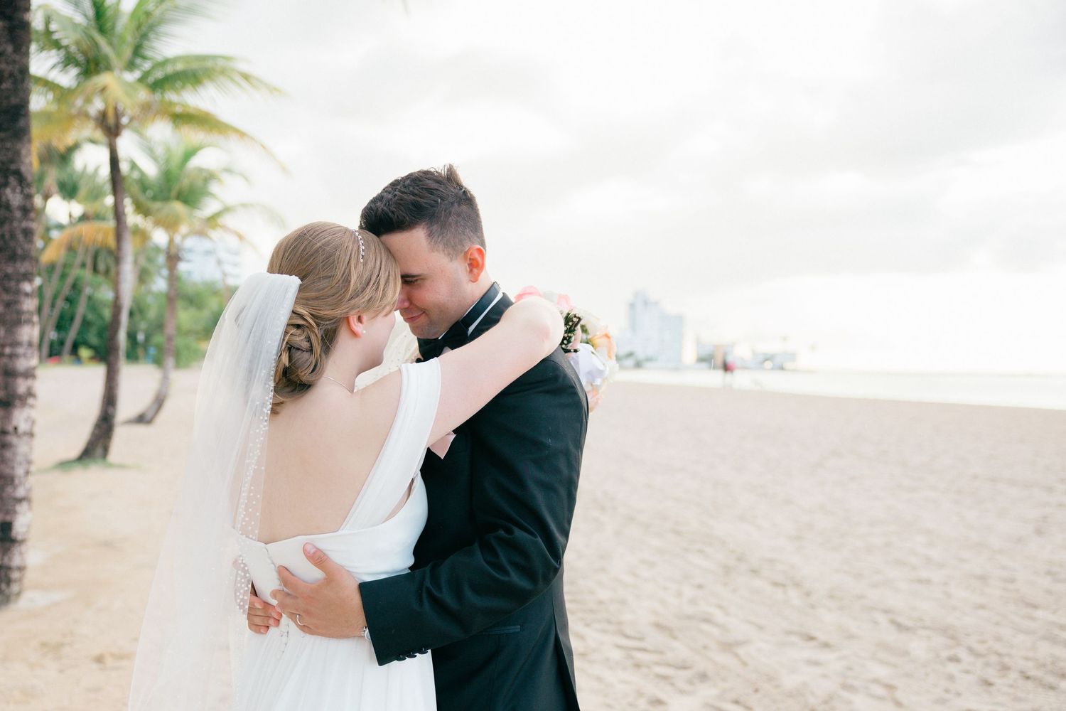 Romantic beach wedding portraits with couple embracing against ocean backdrop.