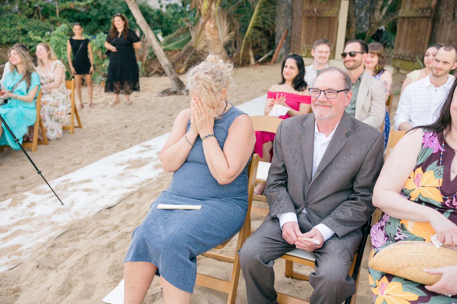 Wedding celebration in lush garden setting with guests seated on wooden chairs.