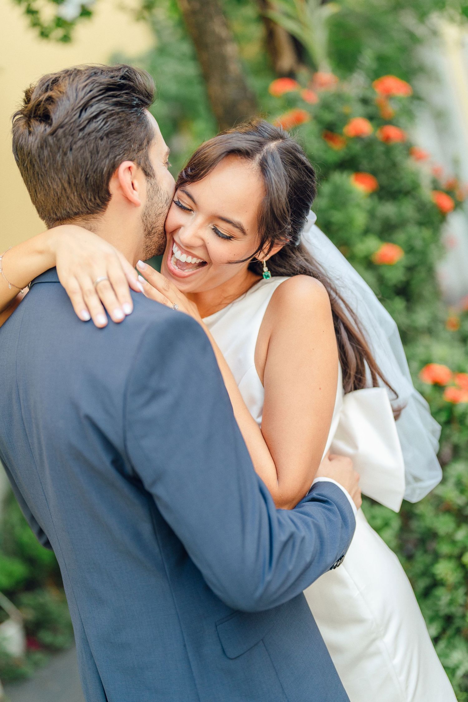 A tender embrace between newlyweds surrounded by lush garden foliage and orange flowers.