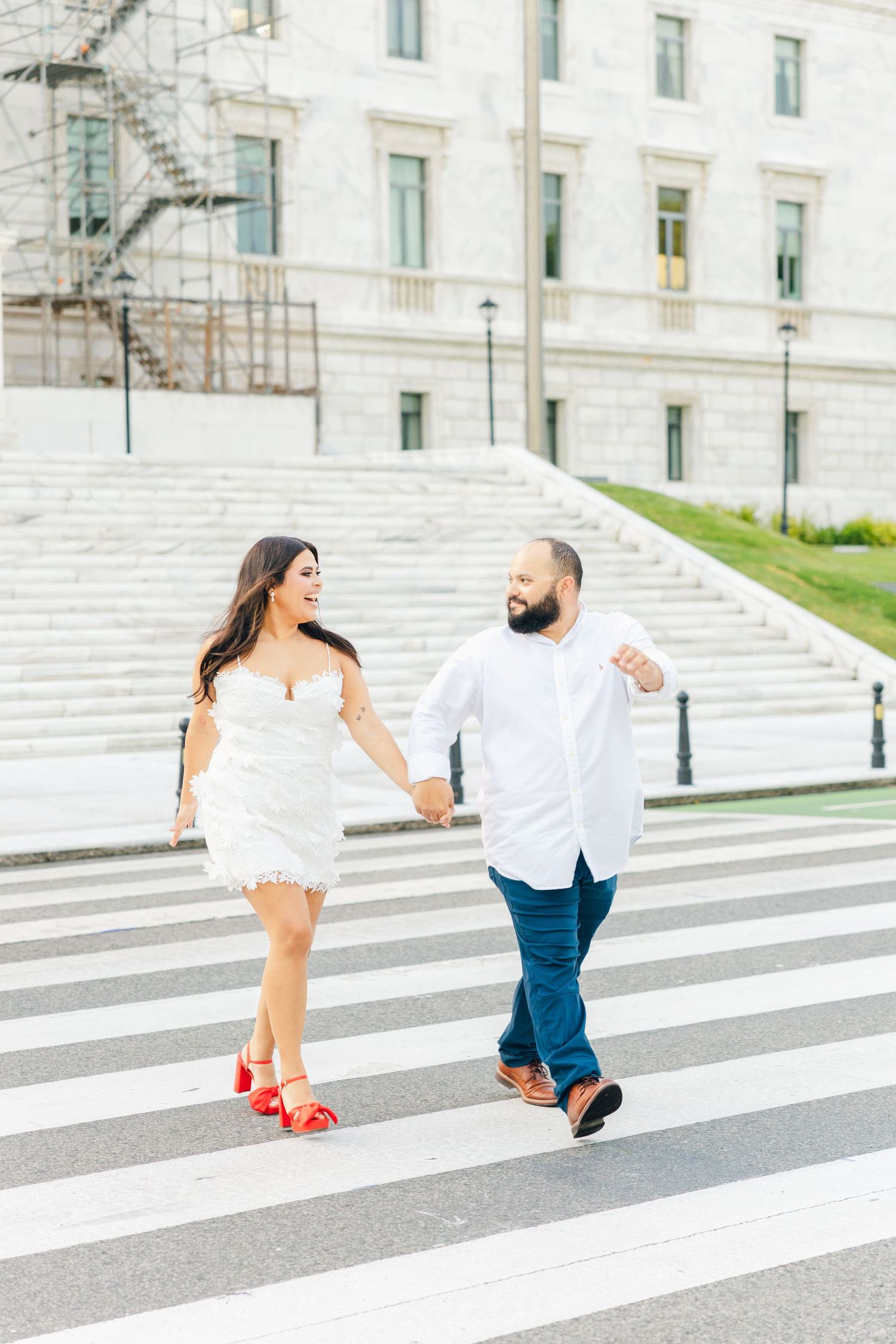 Couple playfully walking across white painted crosswalk stripes.