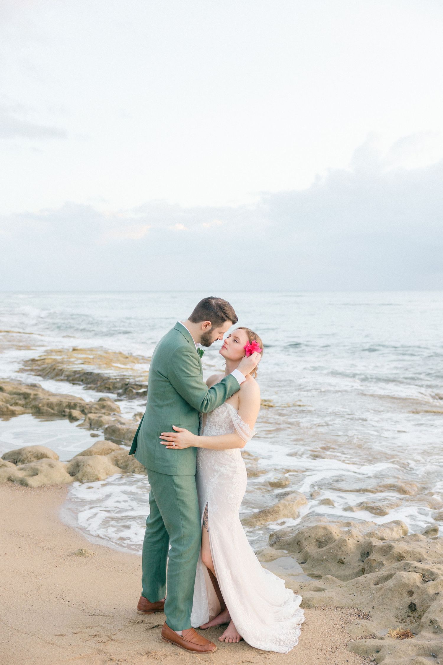 Couple shares romantic moment on rocky beach shoreline at sunset.
