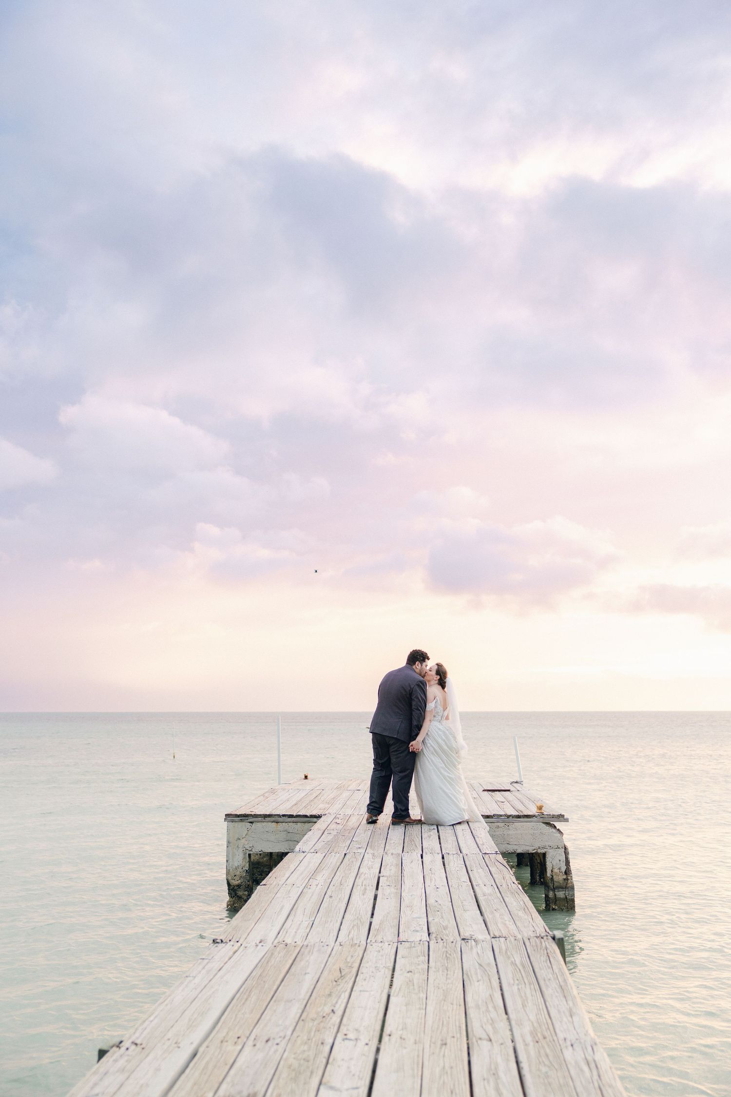 Couple sits together on a wooden pier overlooking a serene ocean view at sunset.
