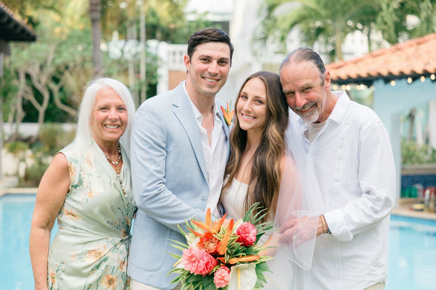 Wedding group photo session by a resort pool with tropical landscaping in the background.