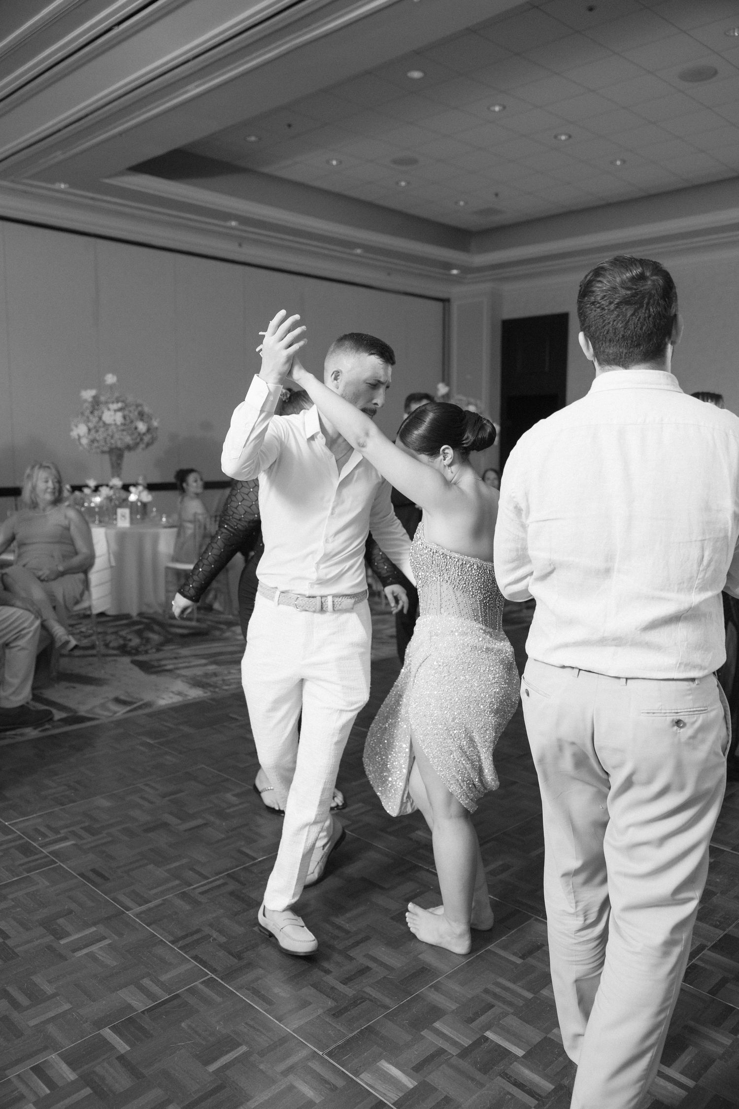 Wedding party members dancing in formal attire on a parquet dance floor.