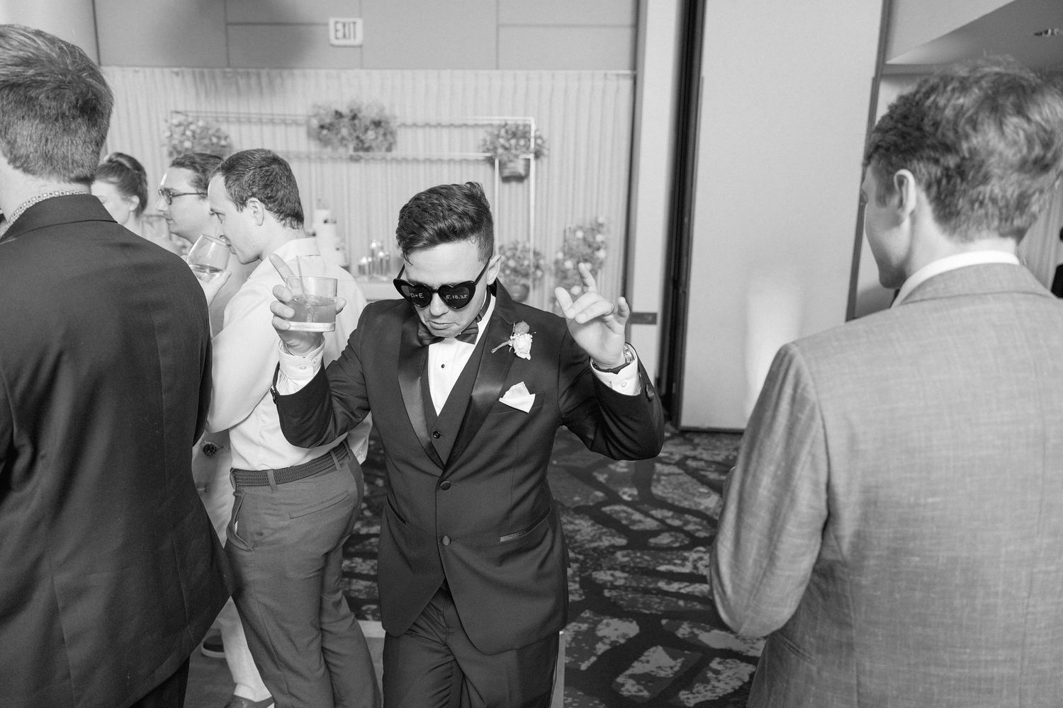 Wedding party members dancing in a line formation at an indoor reception venue.
