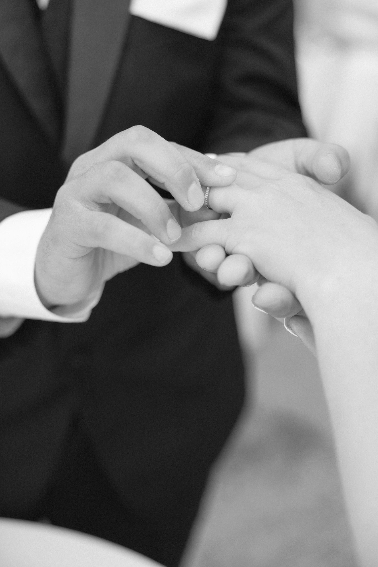 Close-up black and white shots of hands exchanging rings during a wedding ceremony.