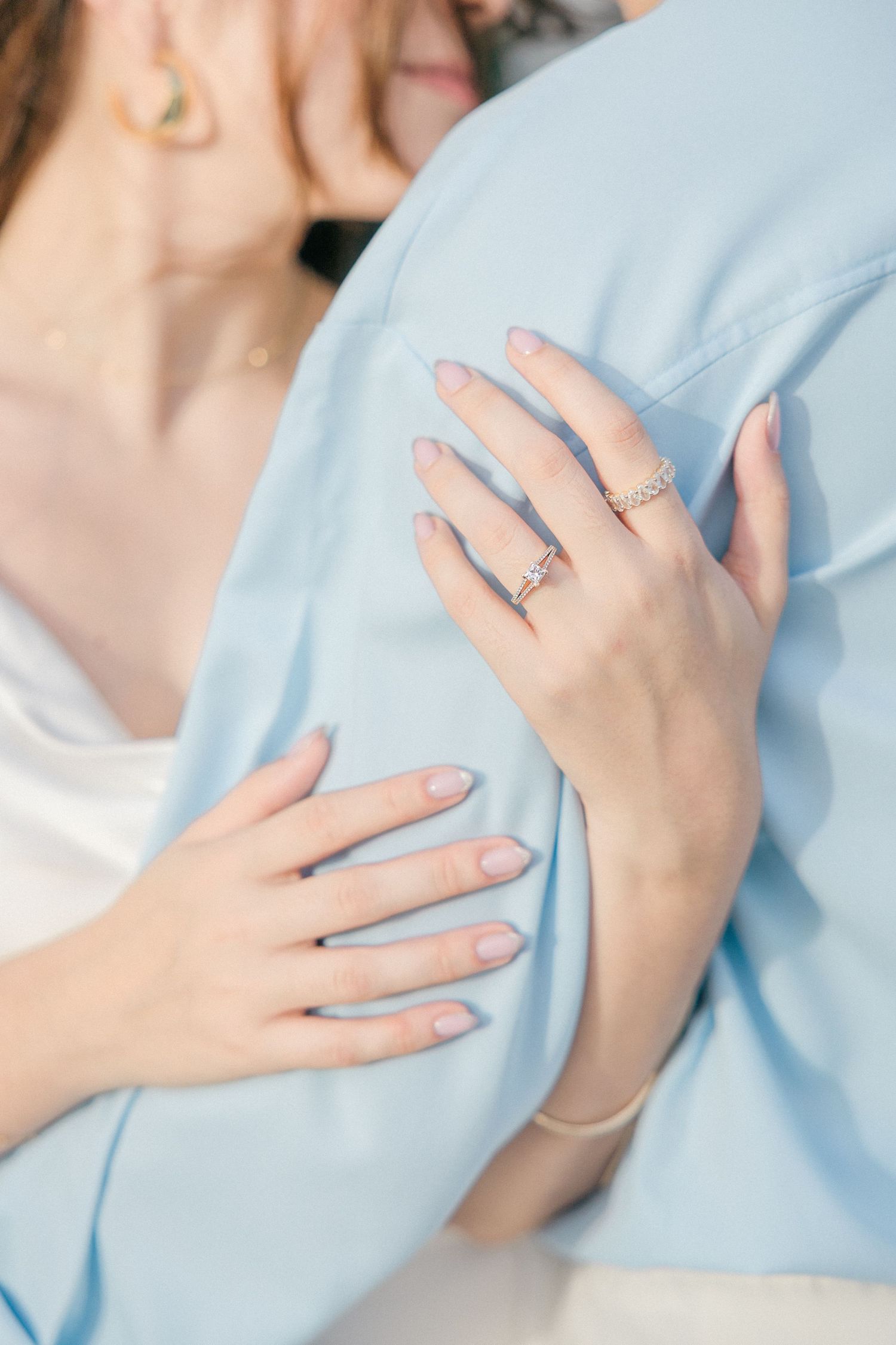 Delicate hands with engagement ring resting on light blue fabric.