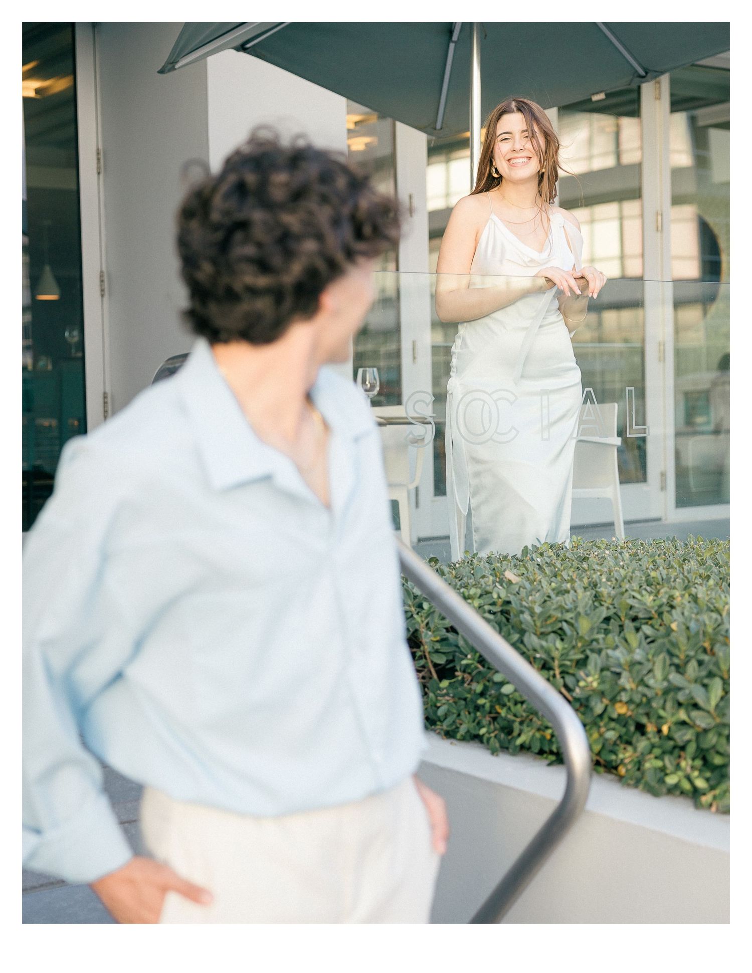 Couple walking together near glass windows and greenery.