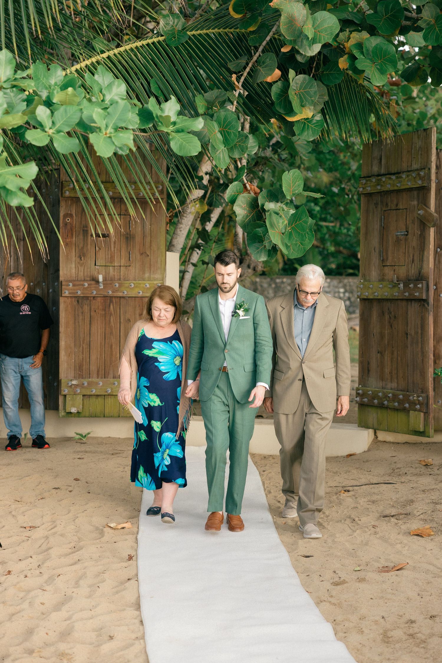 Wedding party walking down palm-lined pathway with tropical foliage backdrop.