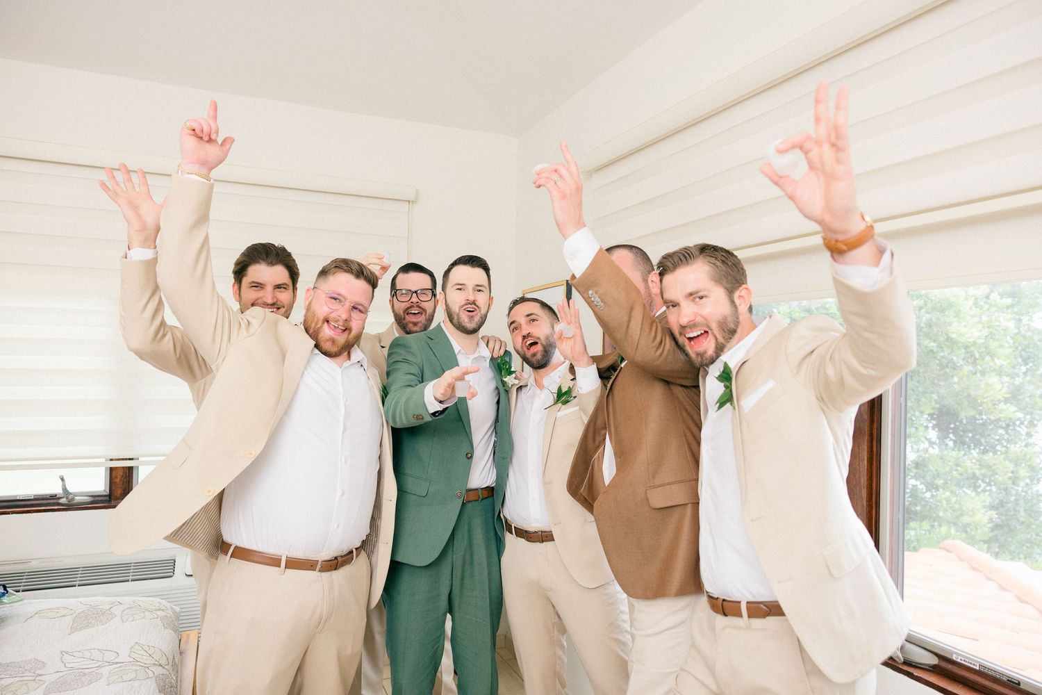 Group of groomsmen in coordinated suits cheering and celebrating with energetic poses.
