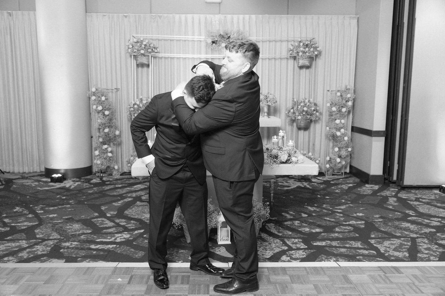 Two people in formal attire embrace playfully at a wedding reception venue.