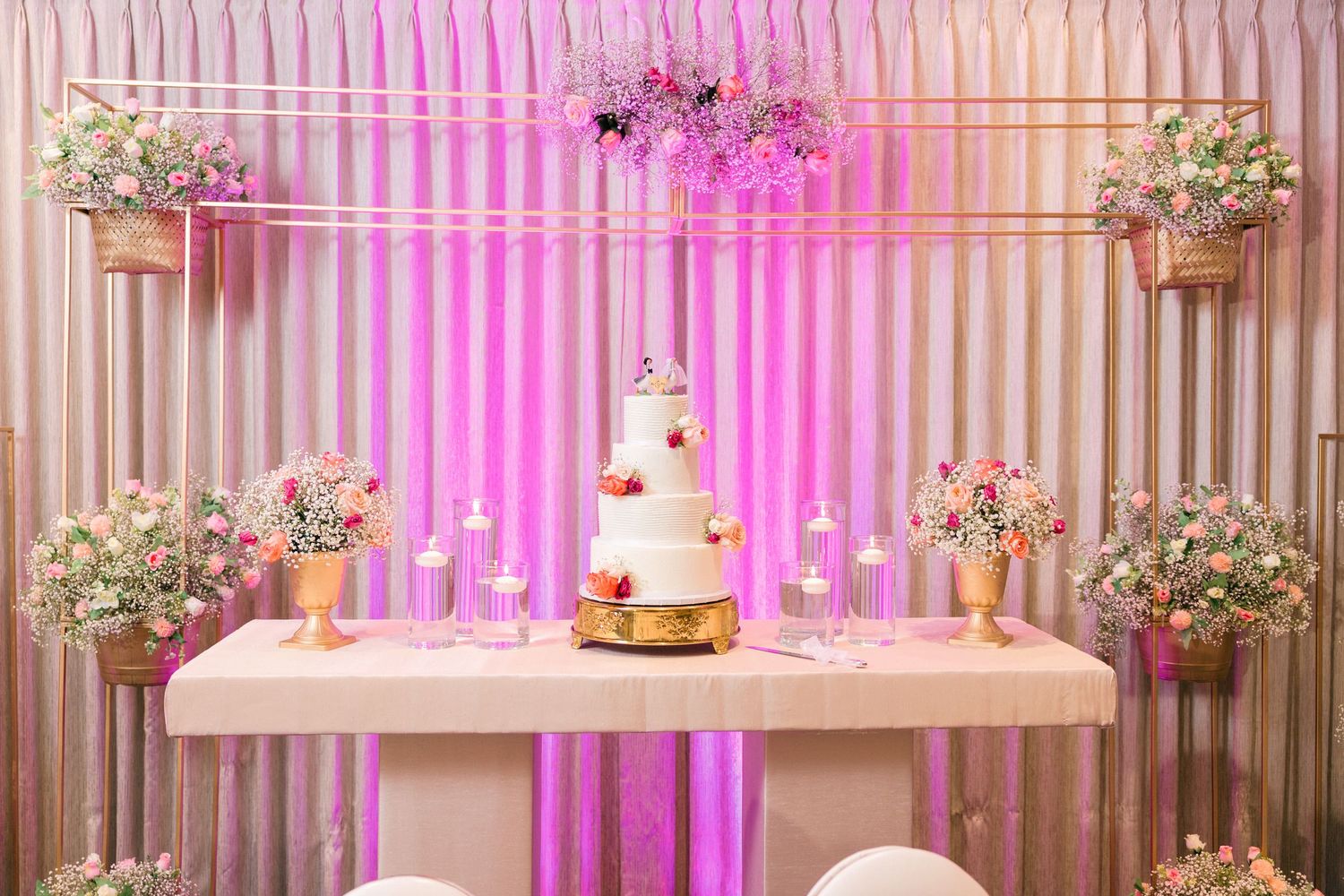 Elegant wedding reception setup with pink lighting and floral centerpieces.