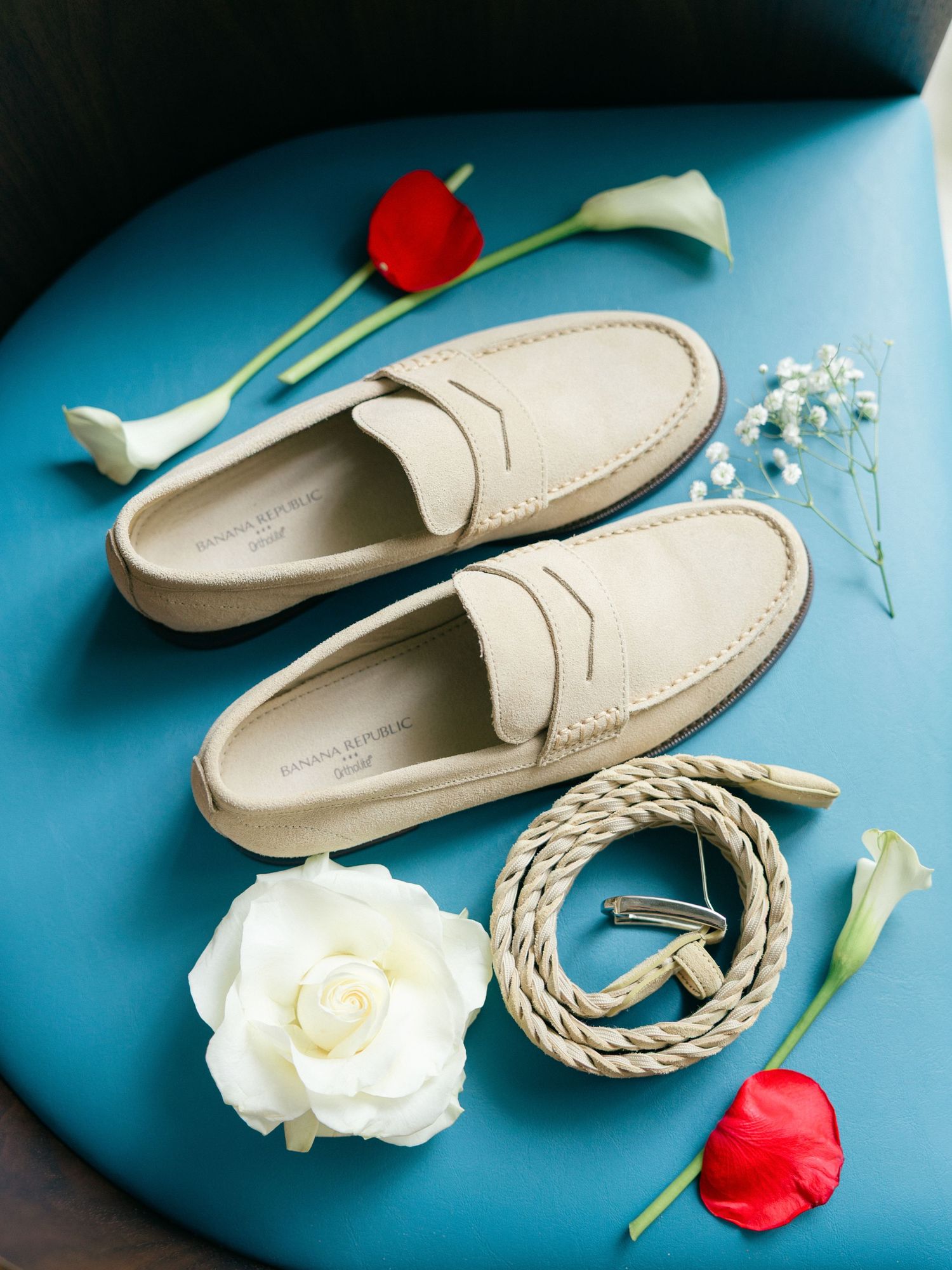 Cream colored loafers arranged with white roses and red tulips on blue background.