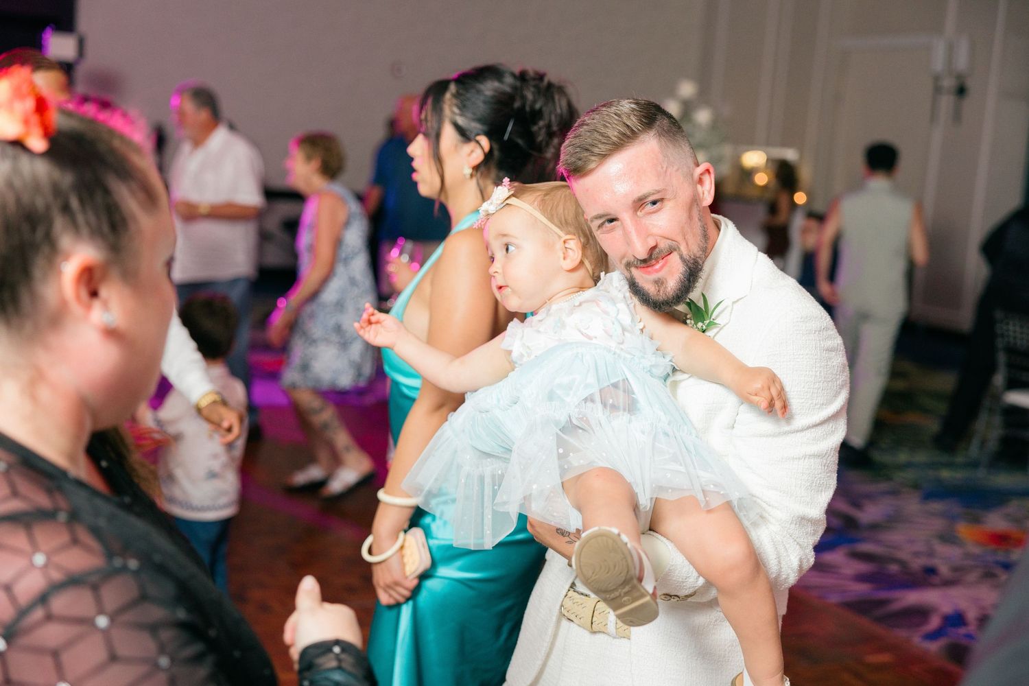 Wedding guests dancing energetically on a colorfully lit dance floor.