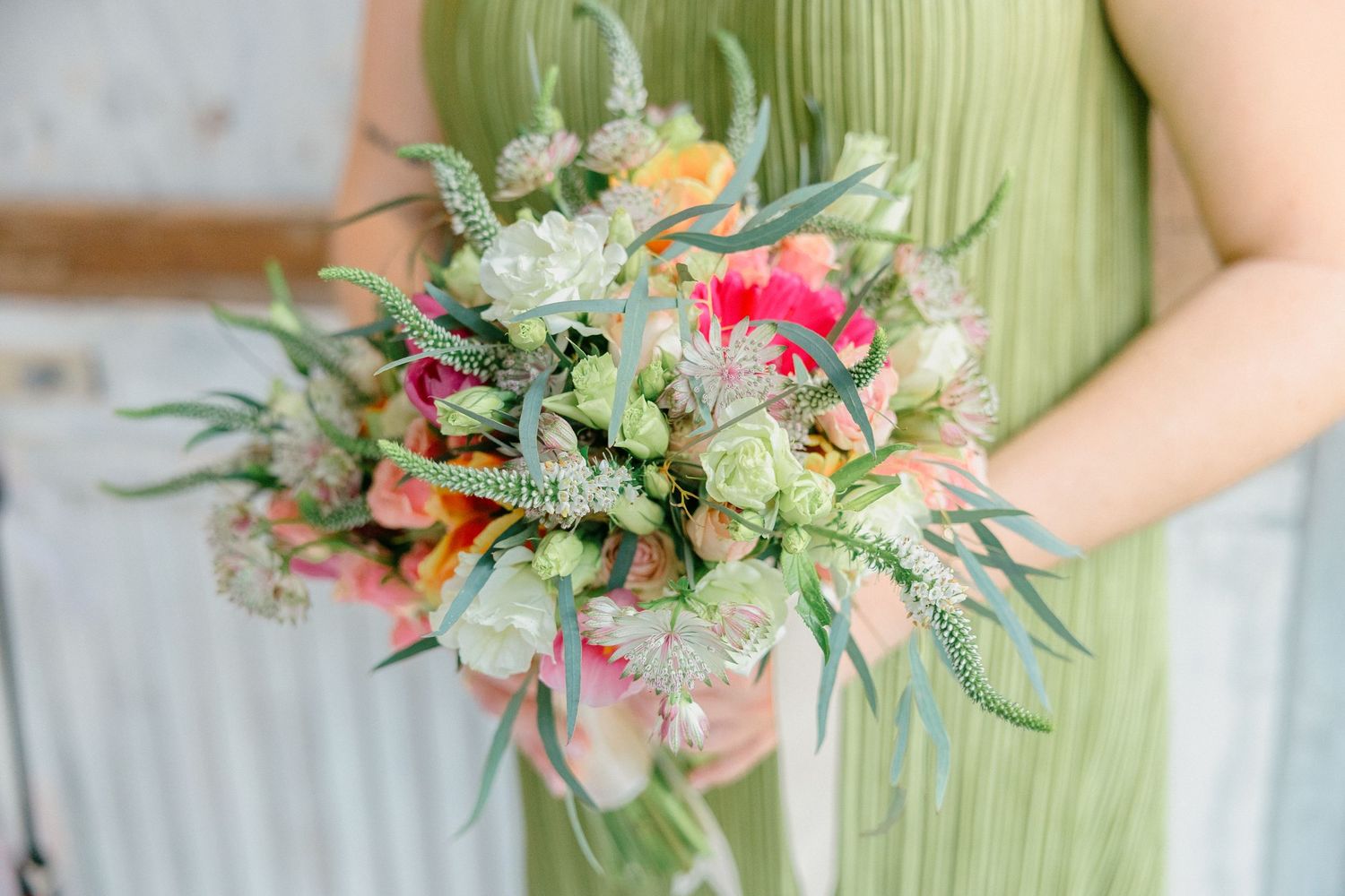 Colorful wildflower bouquet with pink blooms and greenery held against mint green fabric.
