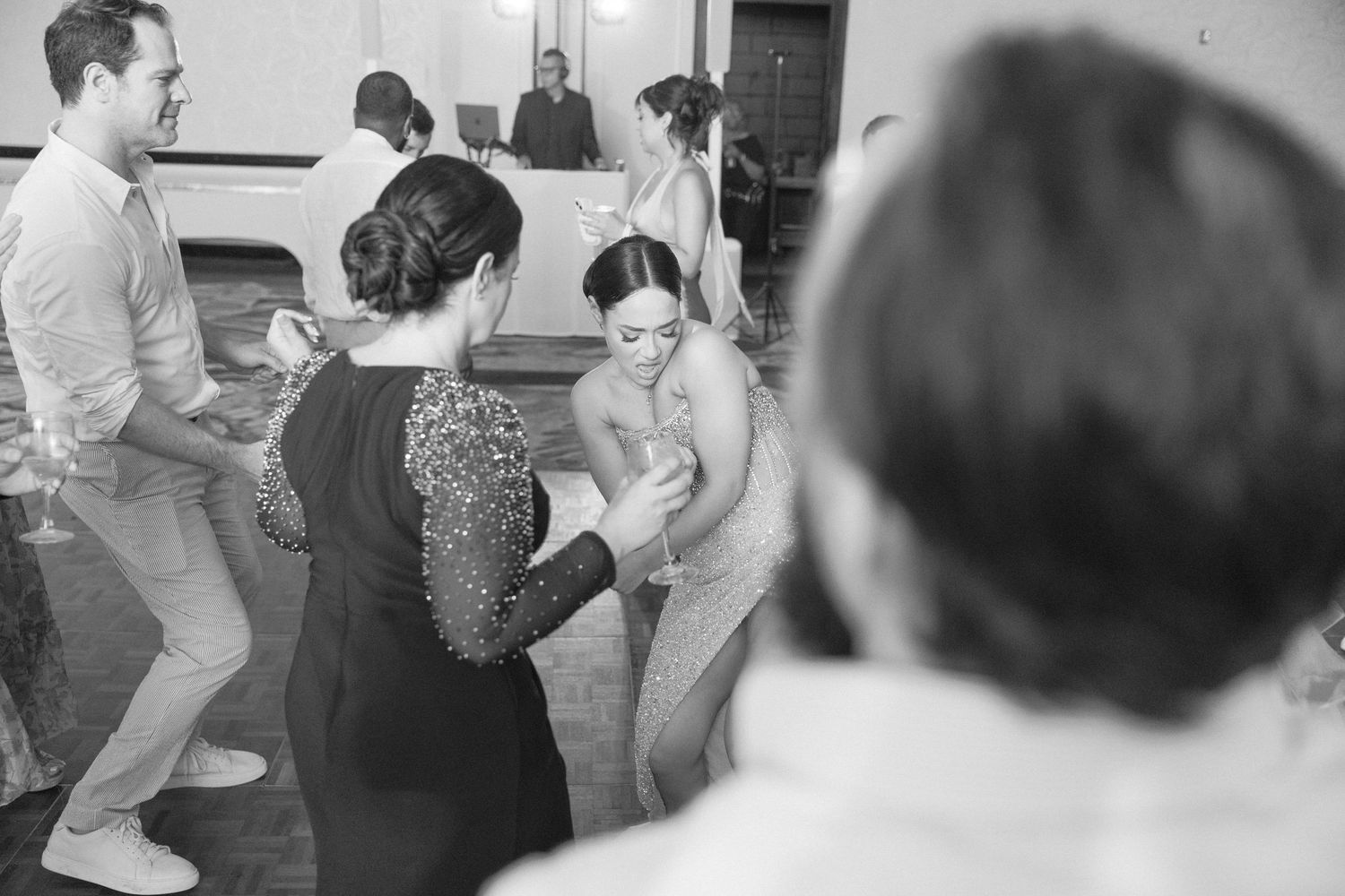Black and white photo of guests dancing at a wedding reception in a banquet hall.