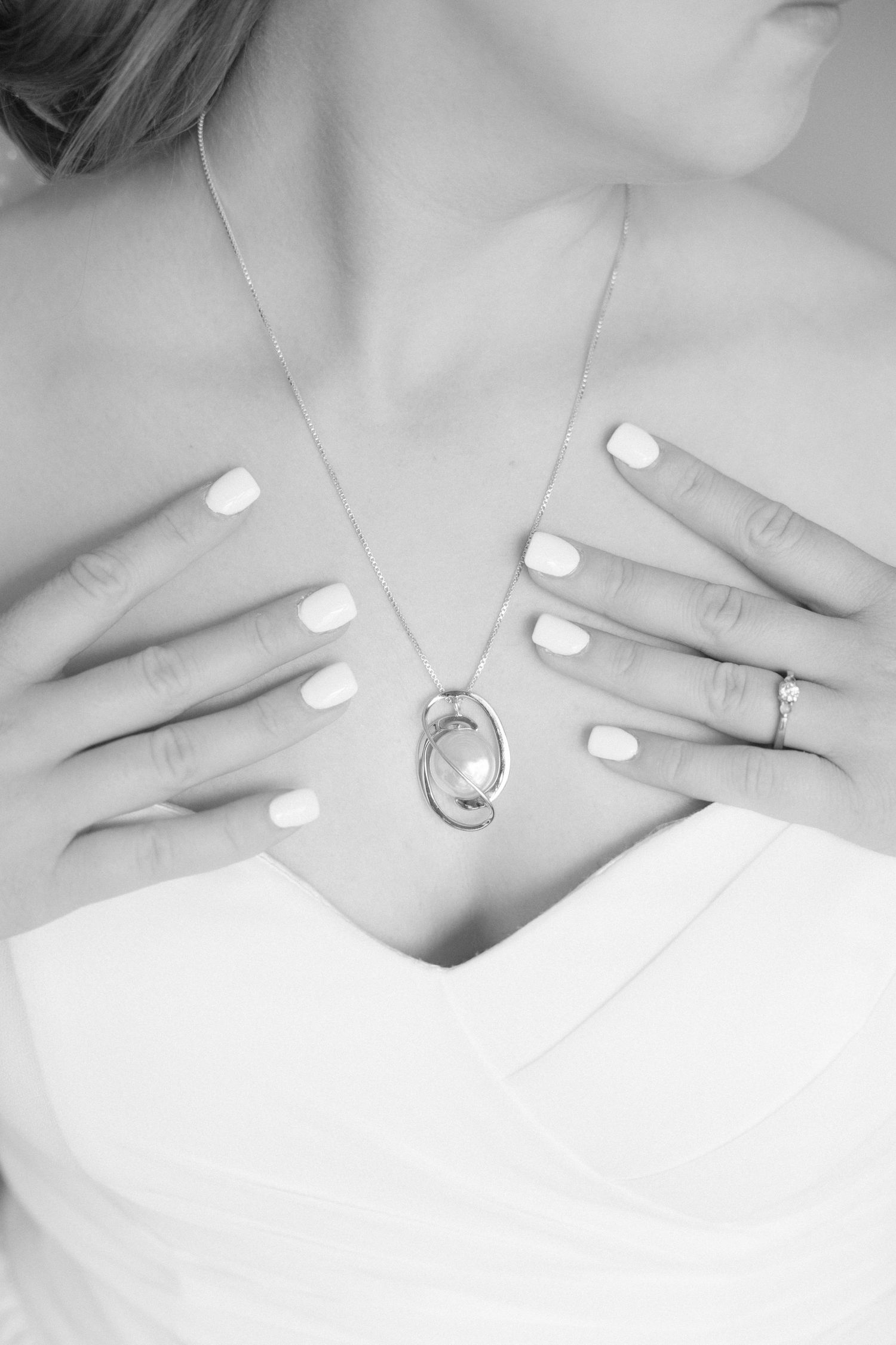Close-up of hands with white manicure and wedding rings against white dress.