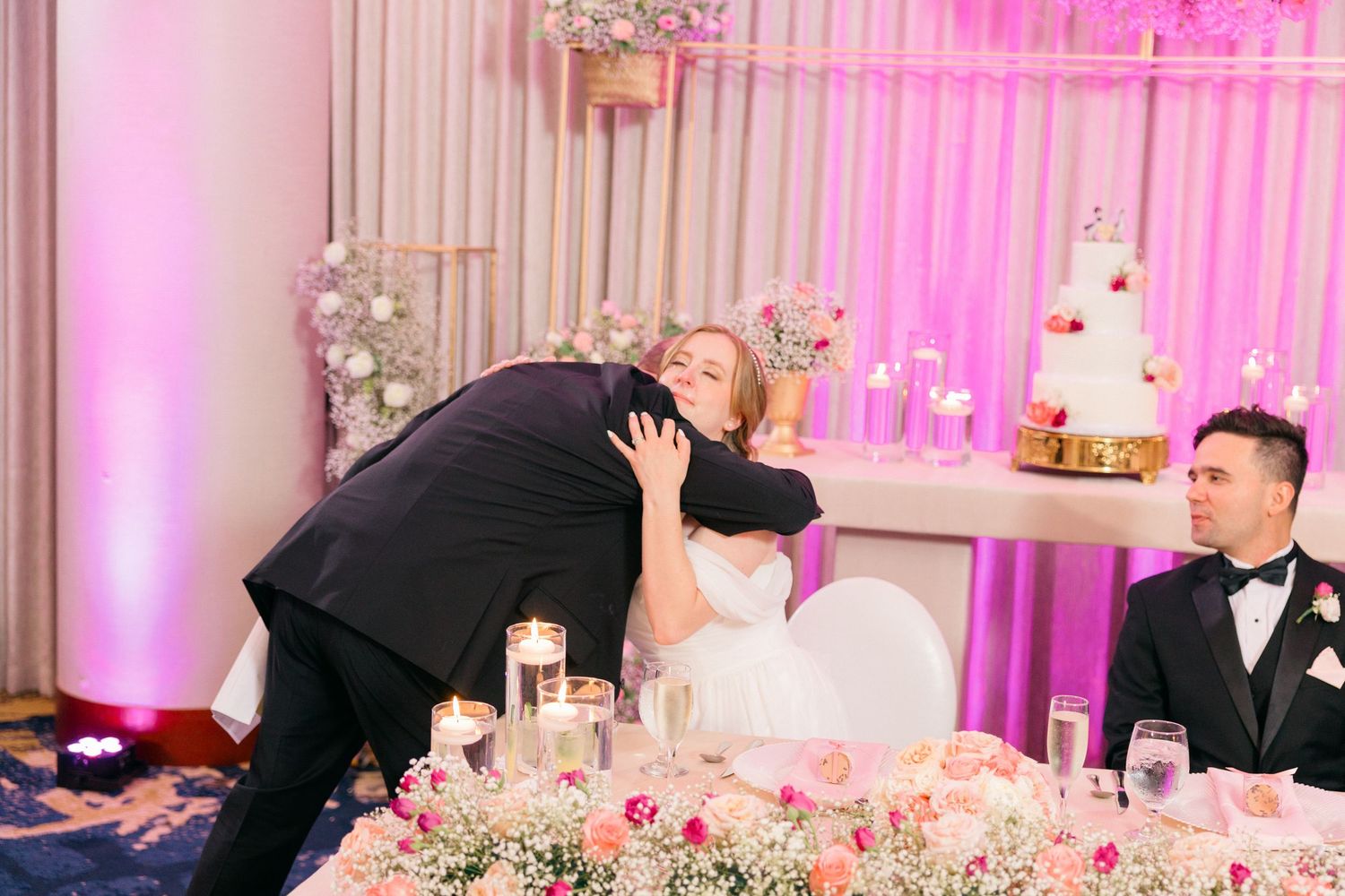 Wedding reception hall with dramatic pink uplighting and white floral centerpieces.