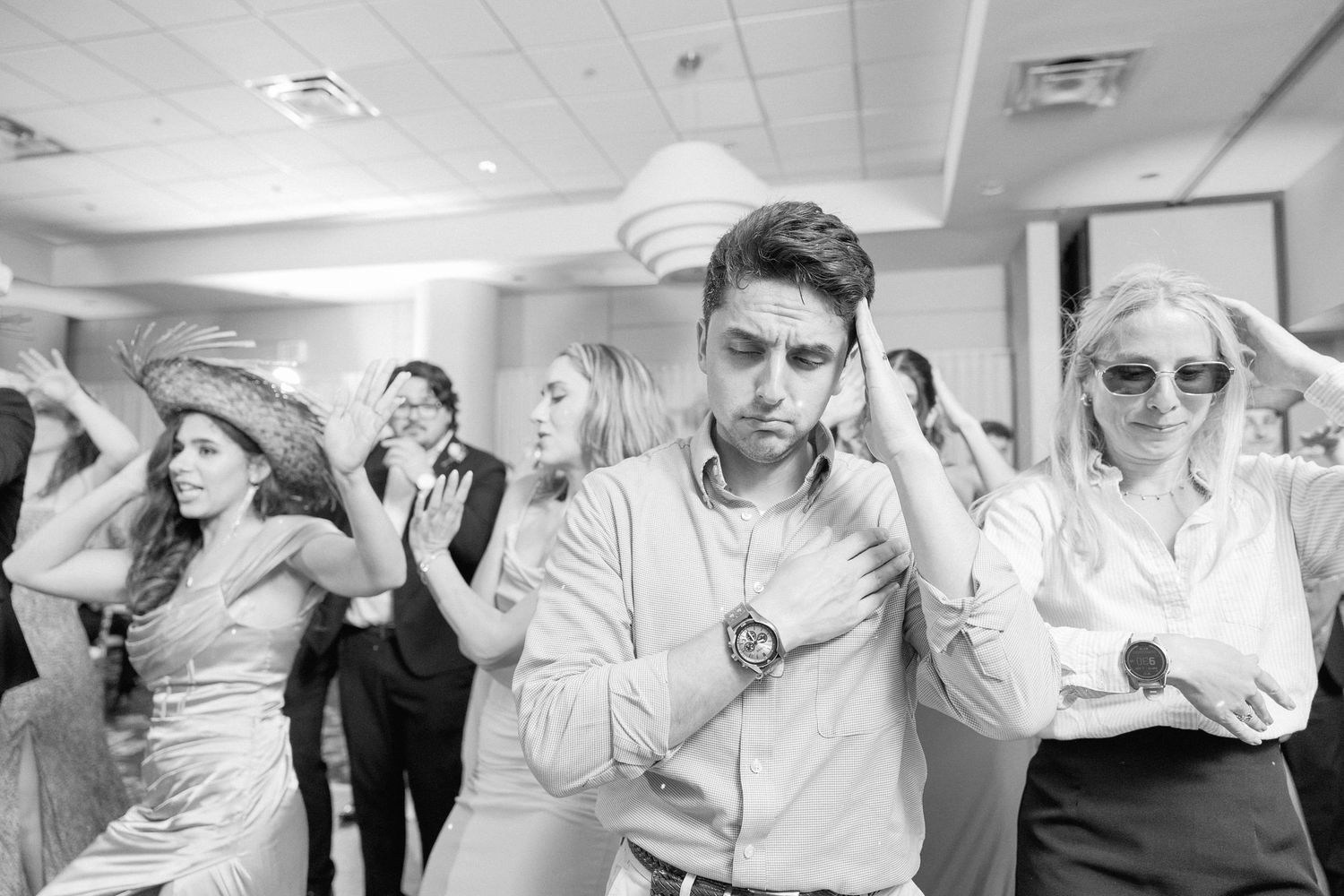 Wedding guests perform choreographed dance moves in sequence at indoor reception.