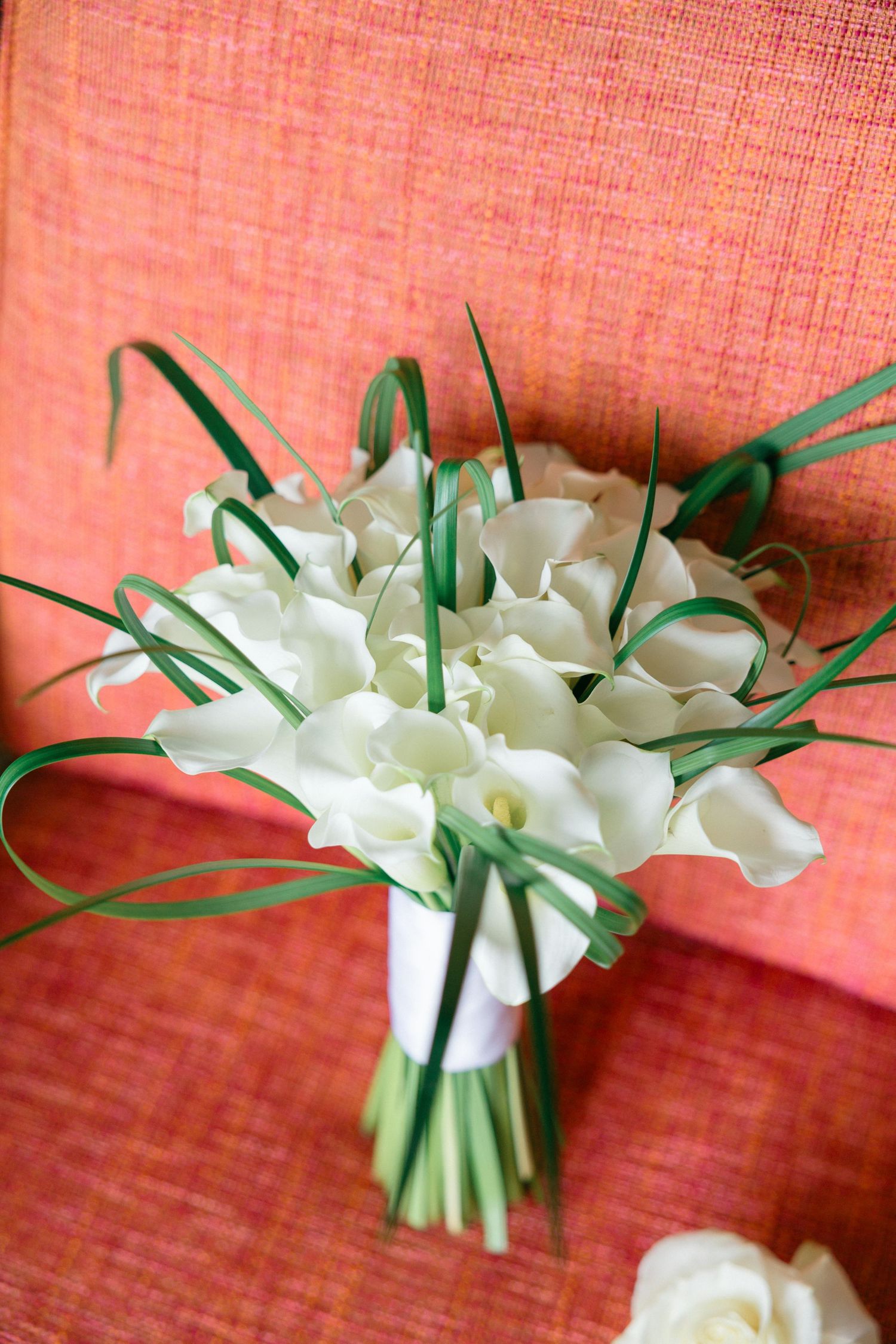 Elegant white calla lily bouquet arranged on coral textured surface.