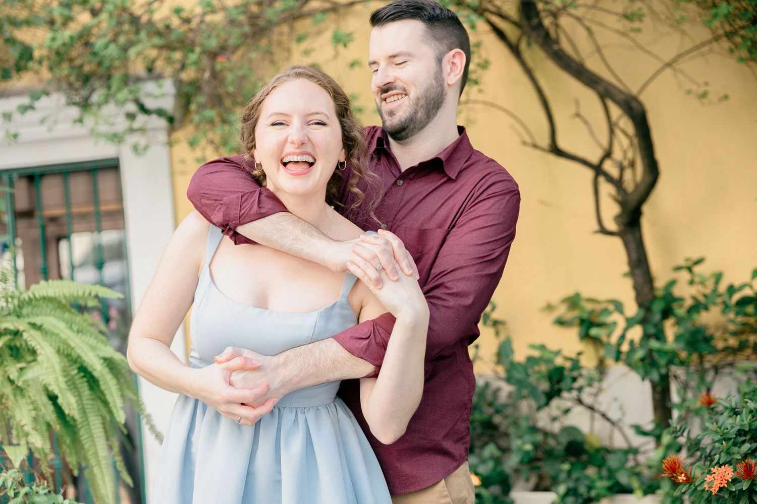 A couple shares a romantic moment in a garden setting with blooming flowers and greenery.
