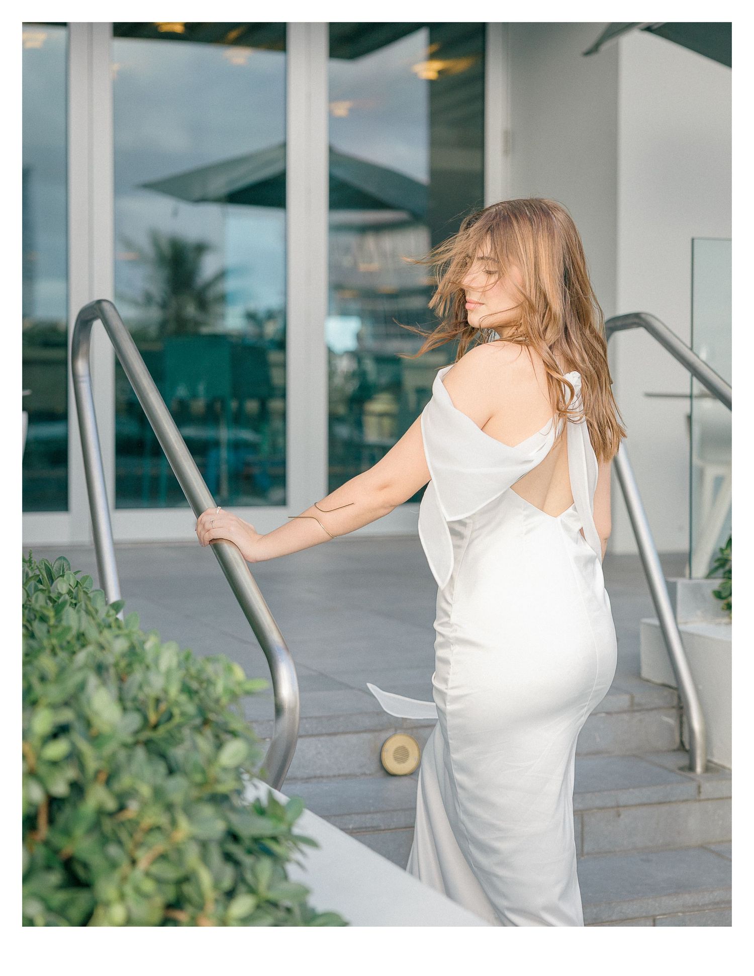 Person in a white sleeveless dress posing near modern architecture.