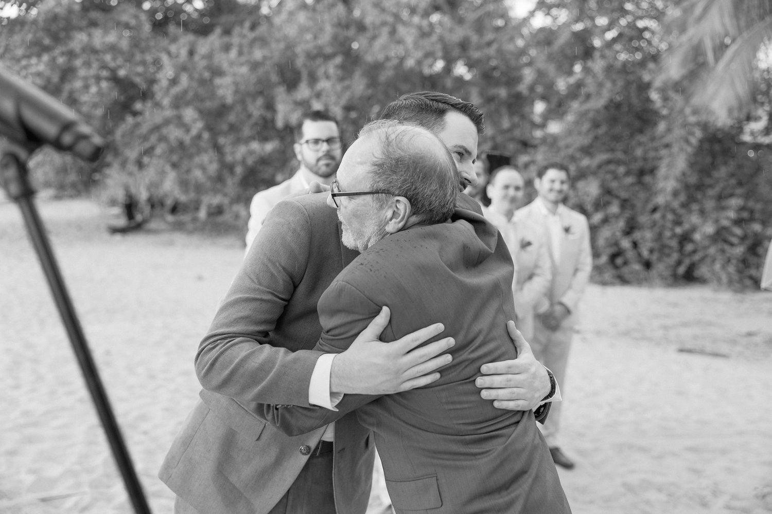 Wedding party members embrace during emotional moments at beach ceremony.