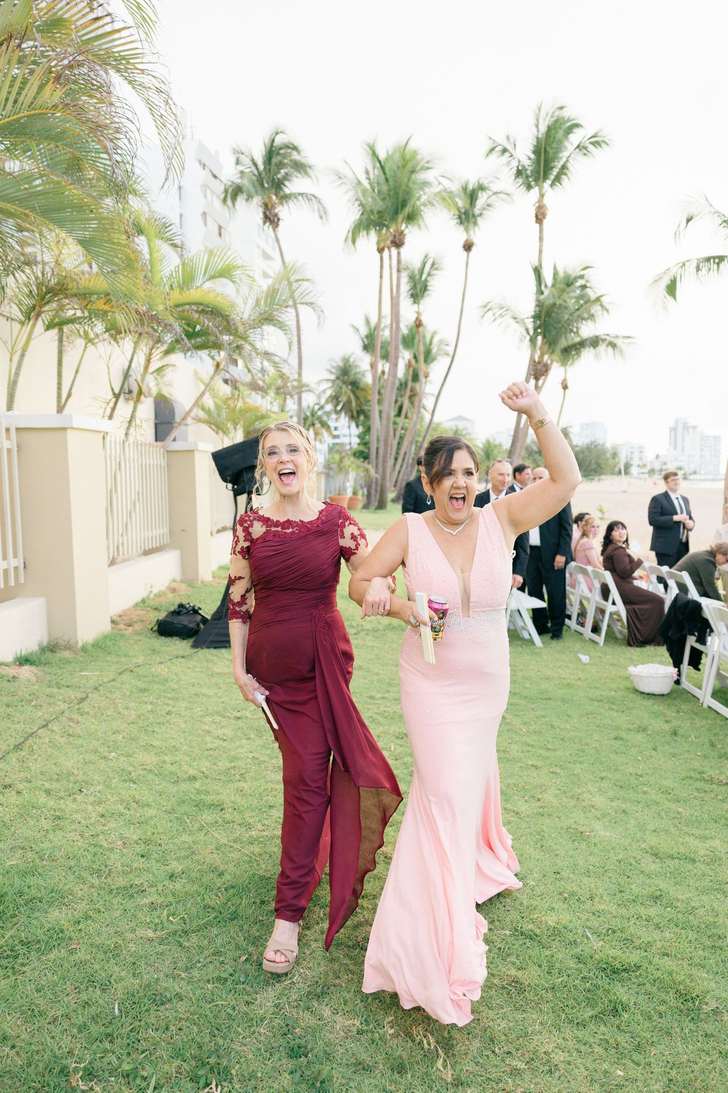 Wedding guests dance joyfully on a grassy lawn with palm trees in the background.