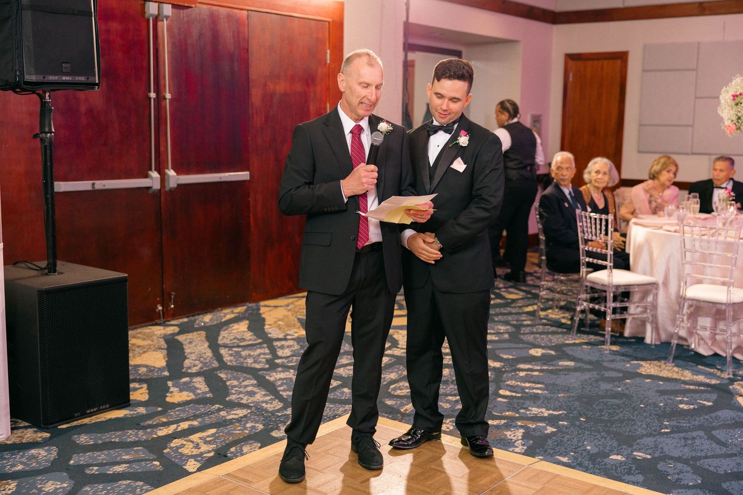 Two people in formal attire stand at a podium during a wedding reception.