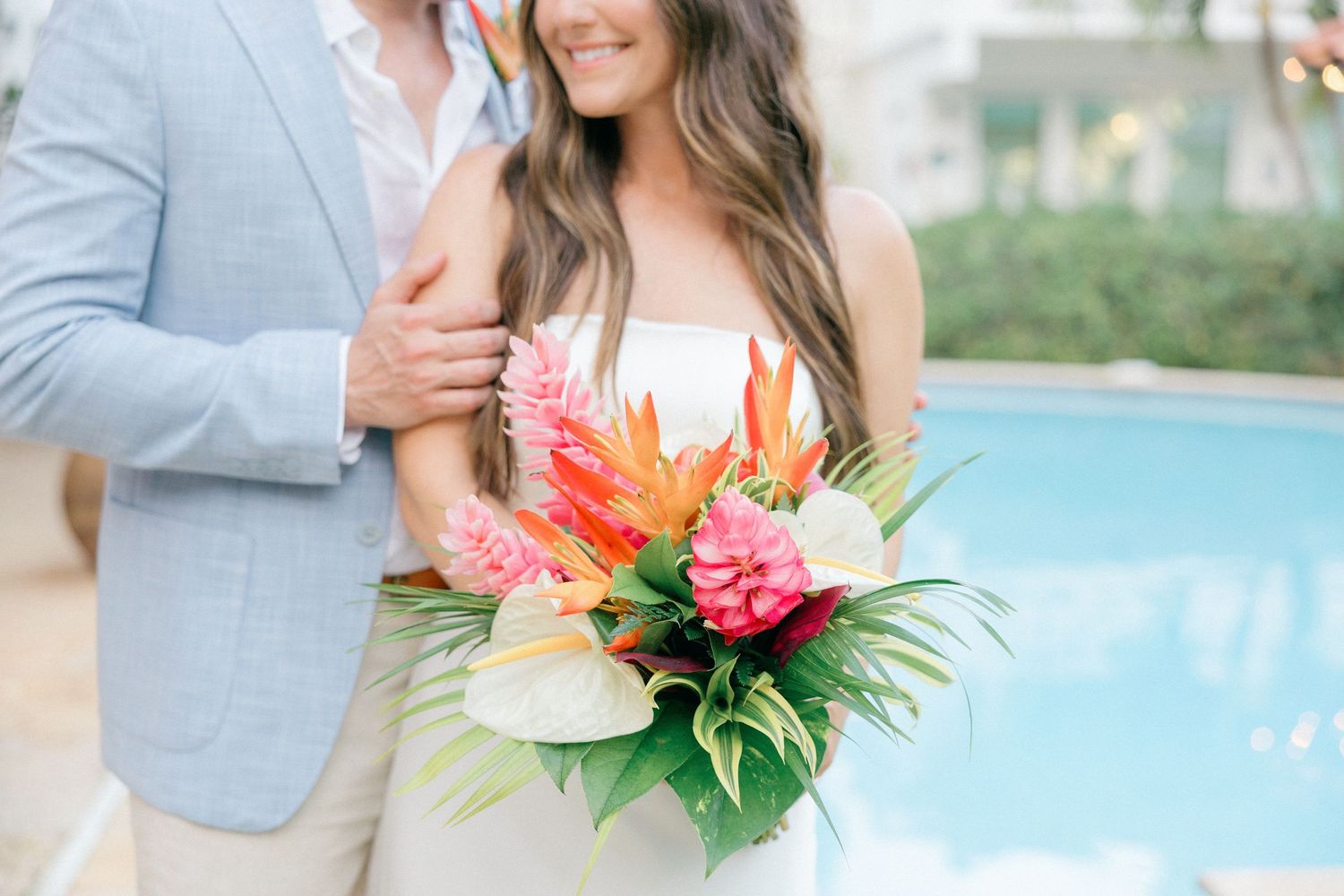 Close-up of couple with tropical bouquet featuring birds of paradise and pink flowers by poolside.
