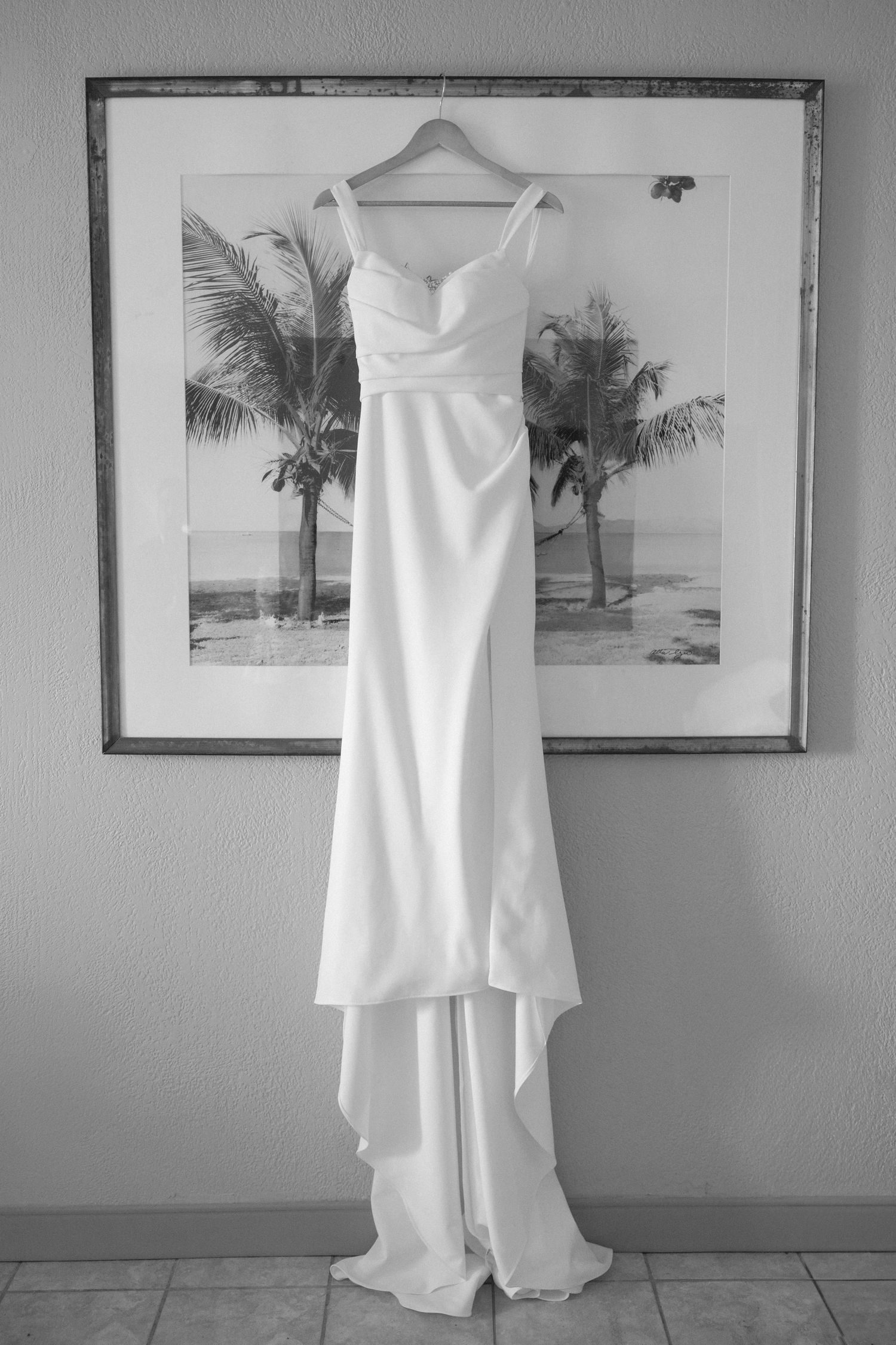 Elegant white wedding dress hanging against wall with beach artwork.