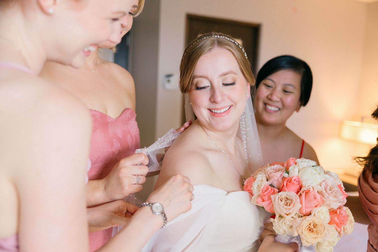 Wedding party getting ready with coral bouquets and elegant dresses in natural light.