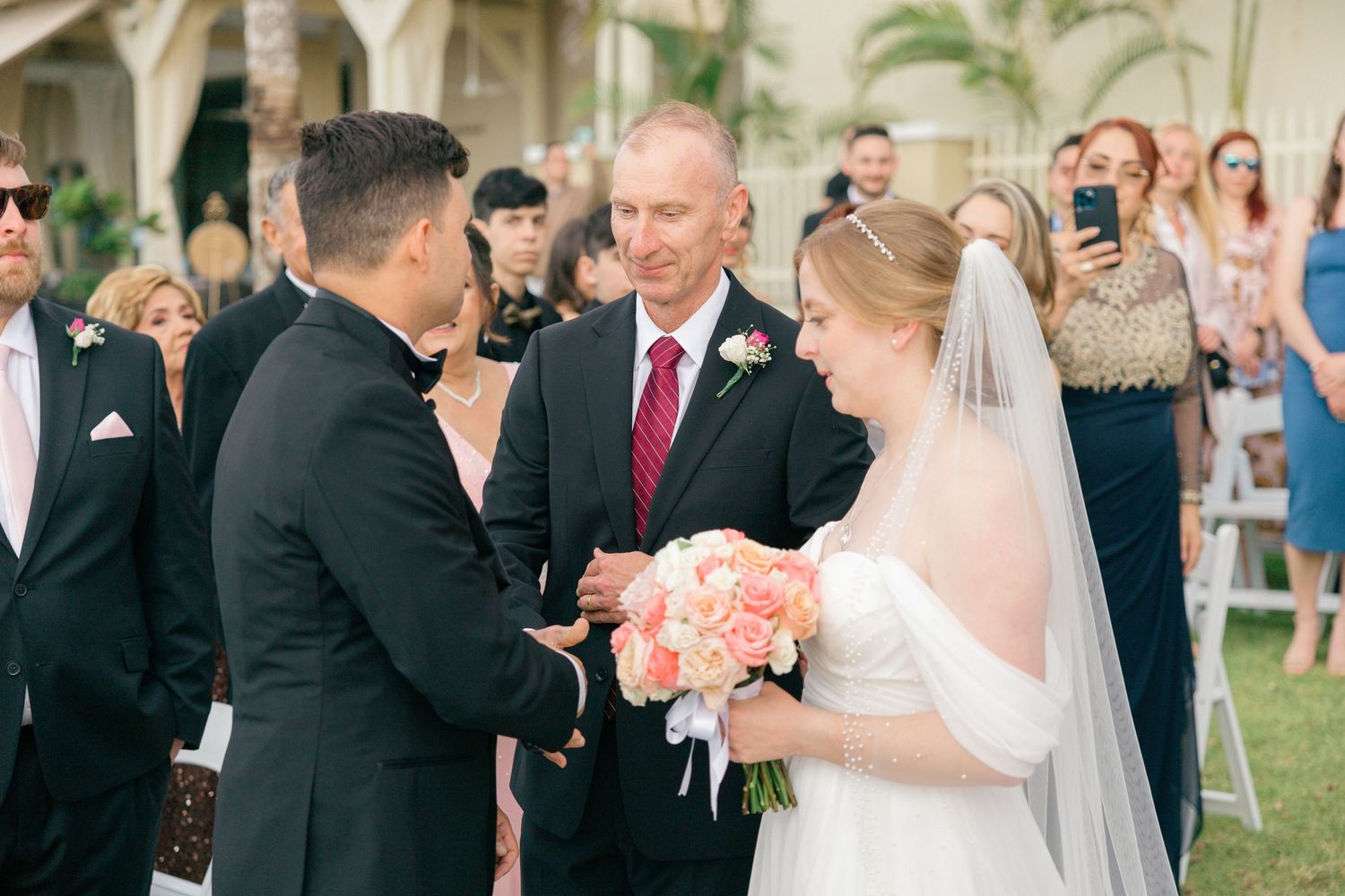Wedding party members gather during an outdoor ceremony with tropical landscaping.