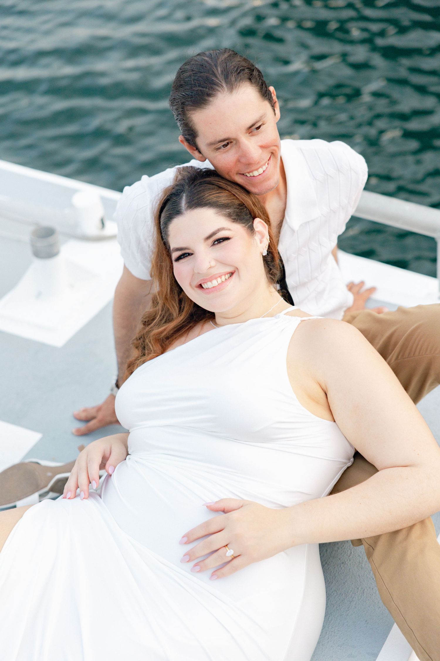 Couple lounging together on a boat deck with turquoise water in background.