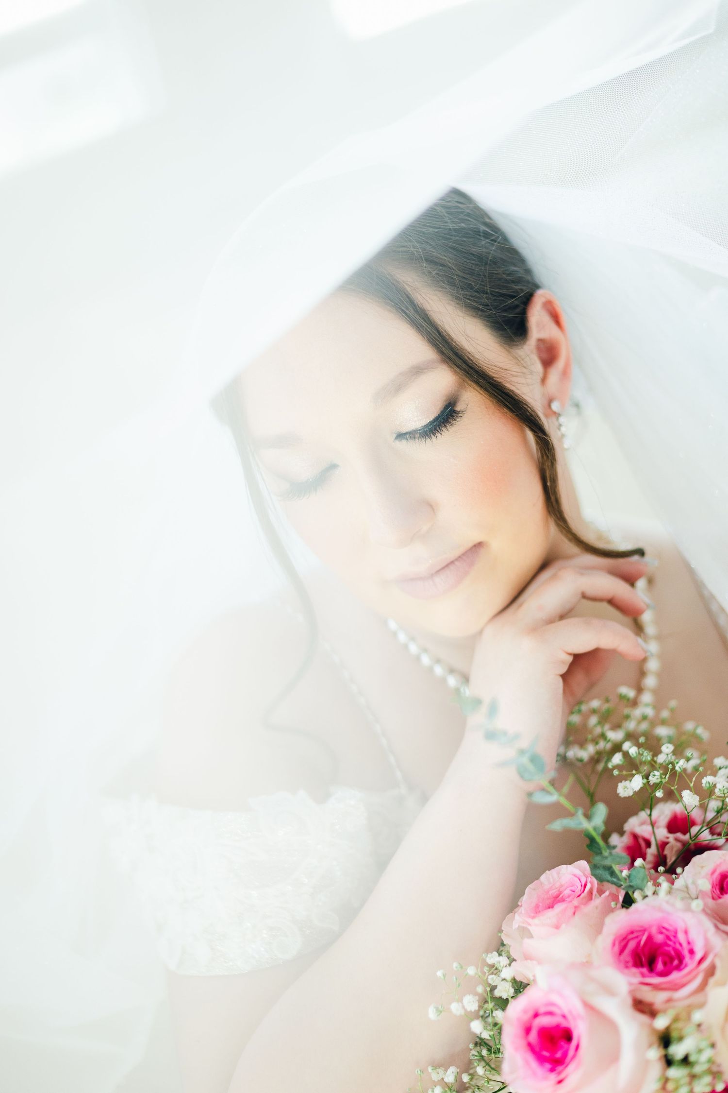 Ethereal bridal portrait with soft lighting and pink roses creating a dreamy atmosphere.