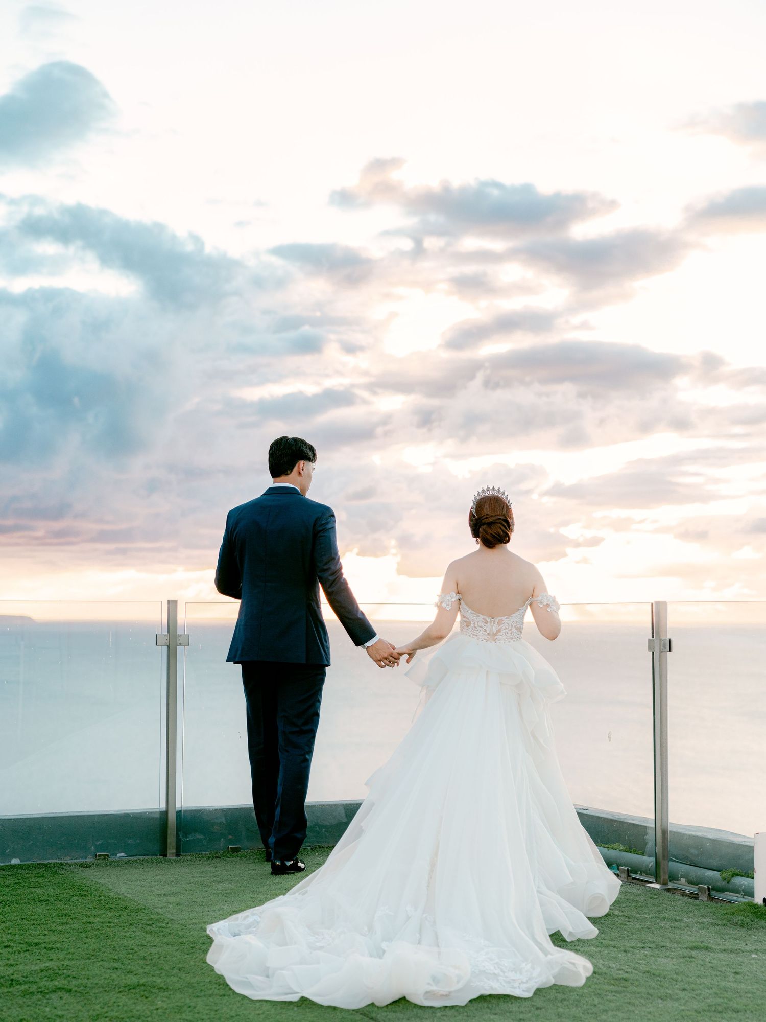 Wedding couple walking hand in hand on a hilltop against a sunset sky.